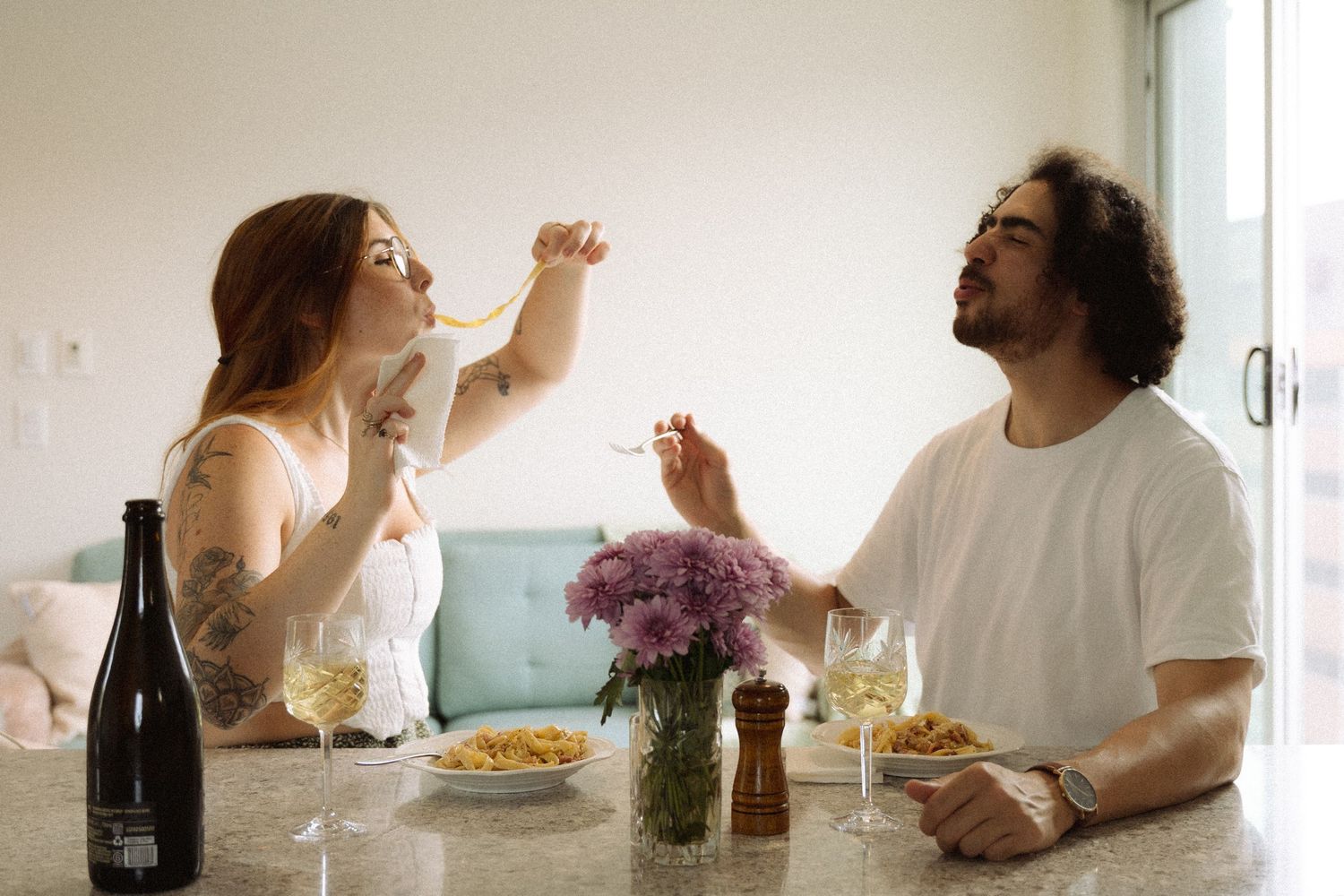 Casual dining scene with wine bottles and plates on a white table in bright interior.