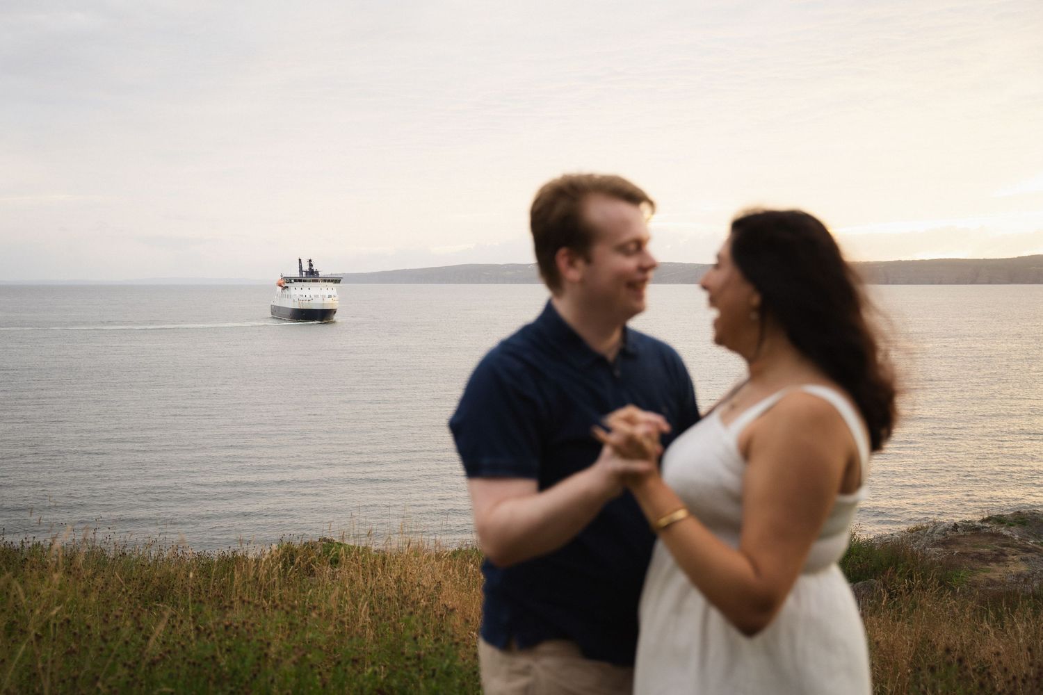 Couple dancing together on a cliff overlooking the ocean at sunset.