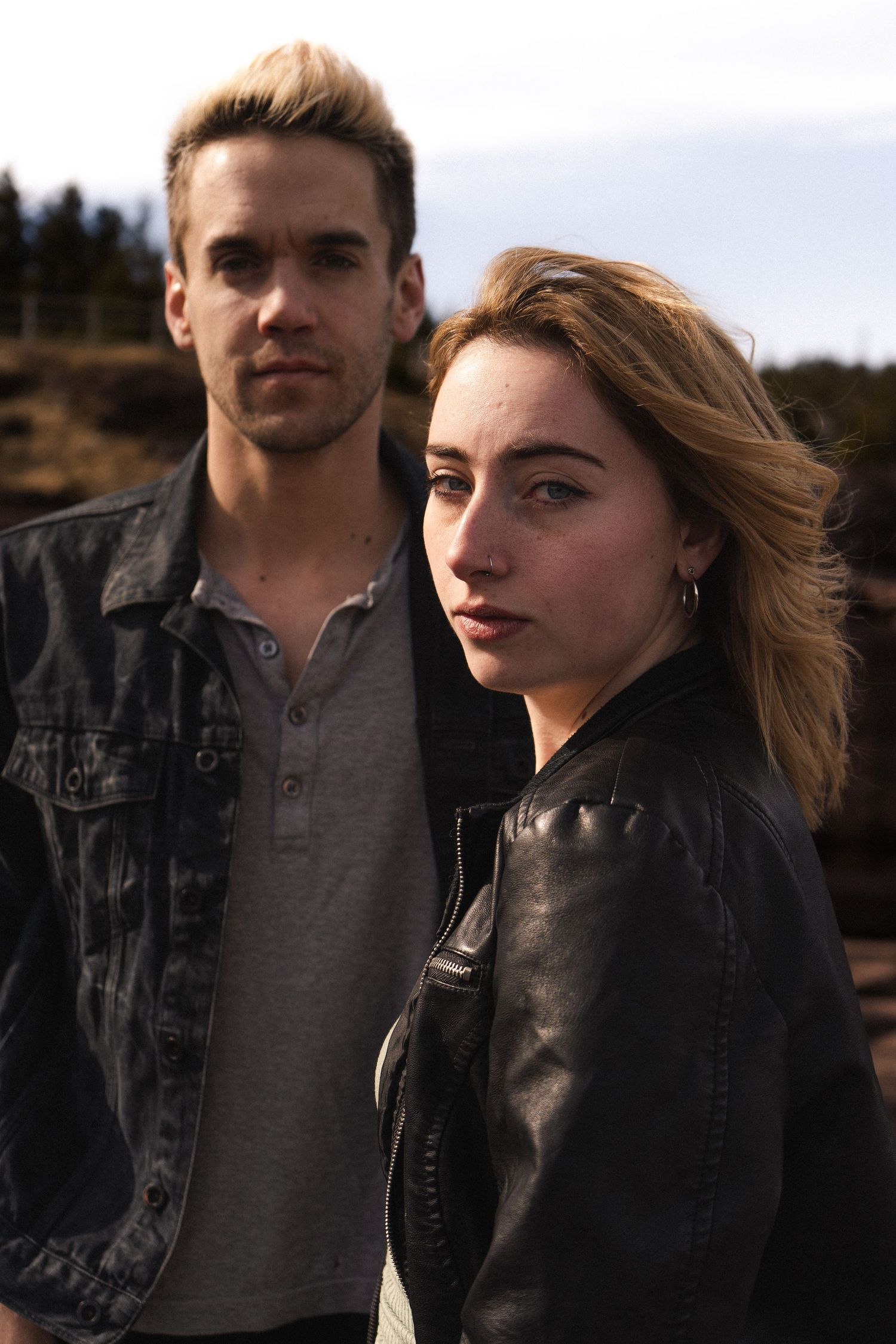 Two people in dark jackets pose against an overcast sky during golden hour.