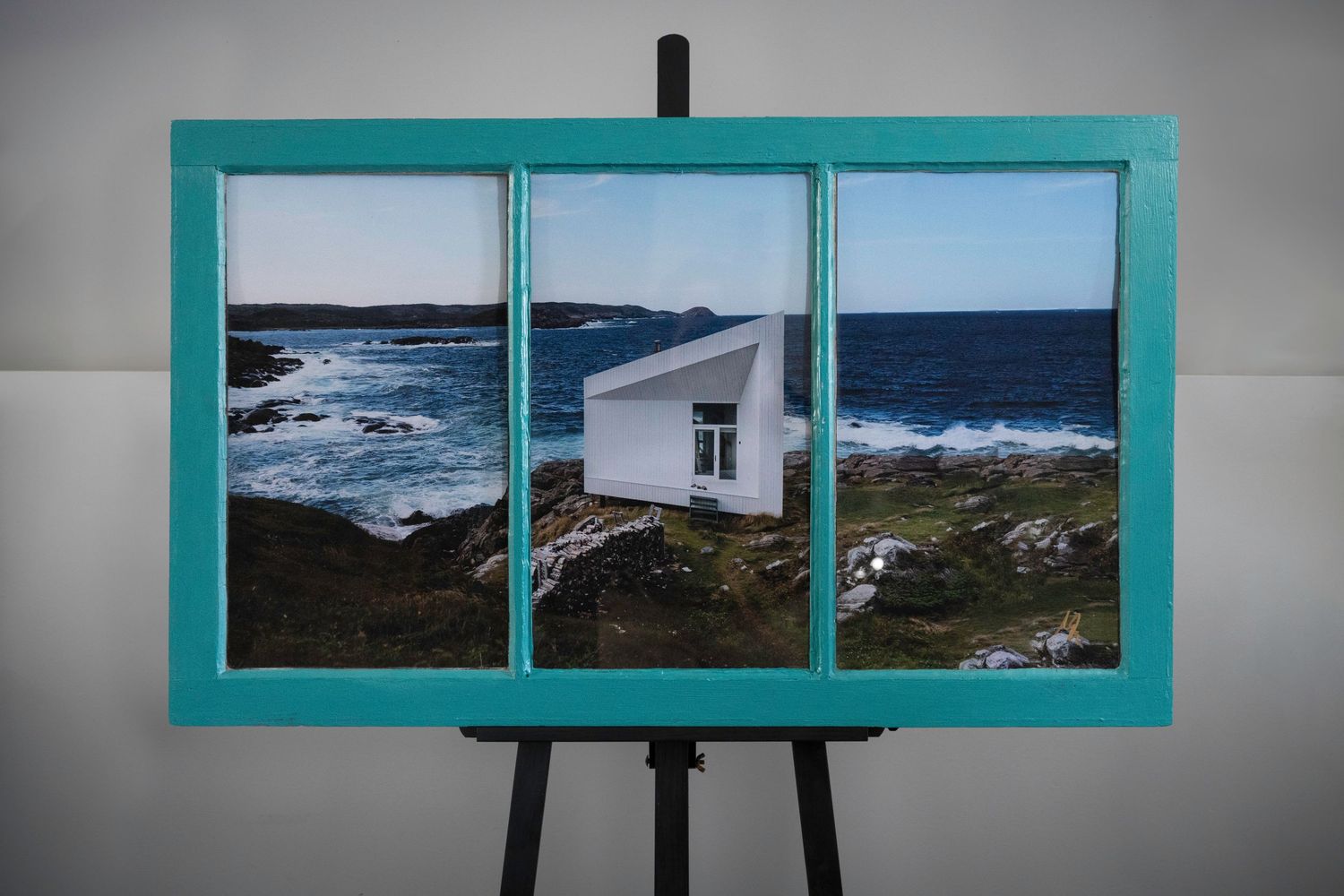 A triptych artwork in a turquoise frame showing a coastal lighthouse scene.
