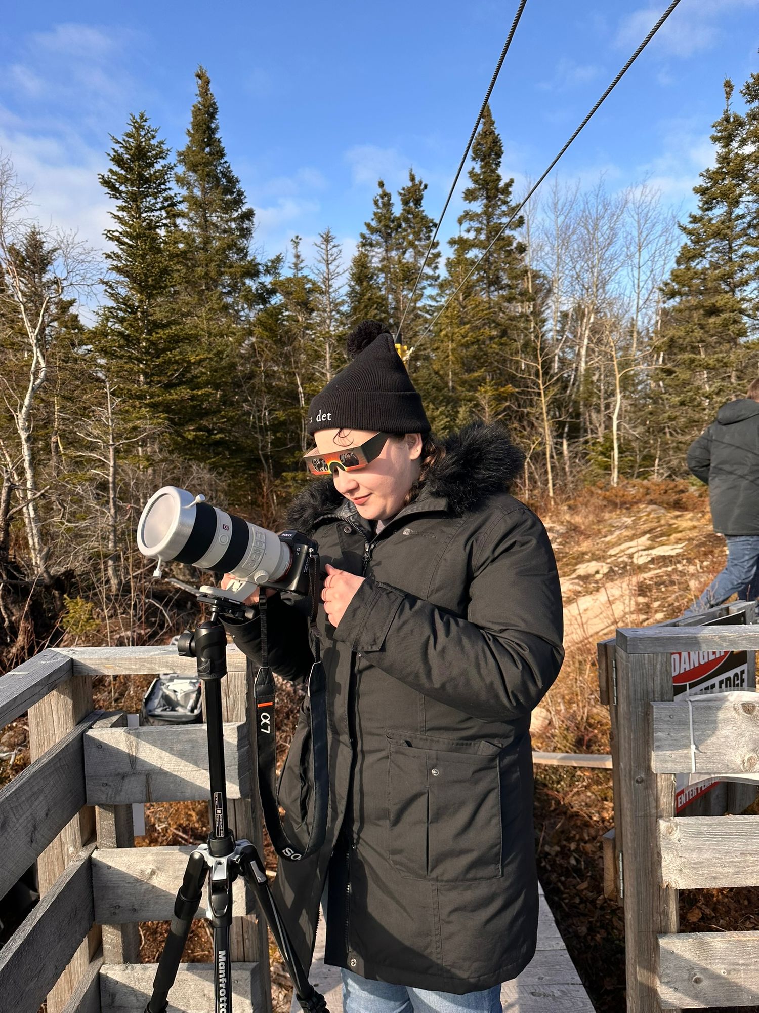 Photographers with telephoto lenses set up on a wooden deck to capture the solar eclipse.