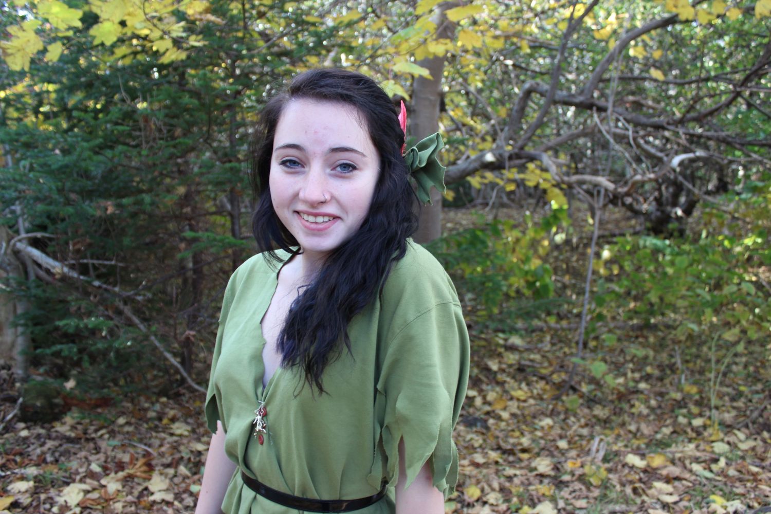 Figure in olive green shirt sits casually outdoors among autumn foliage.