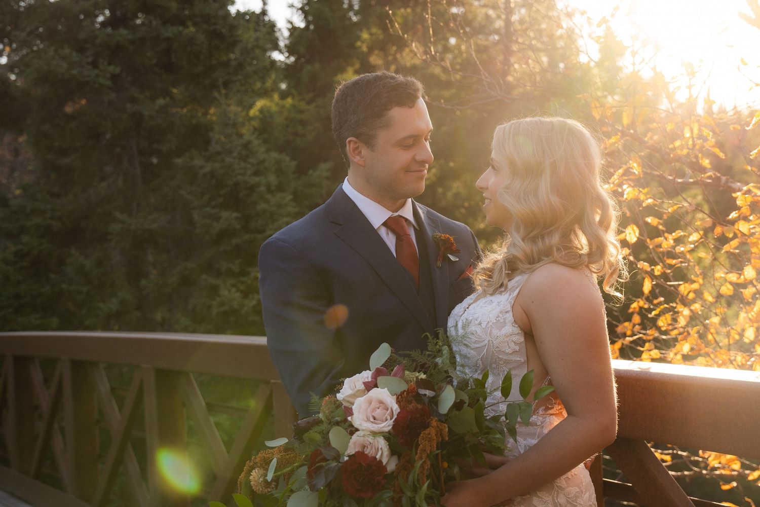 Romantic wedding couple embracing in golden sunset light with floral bouquet.