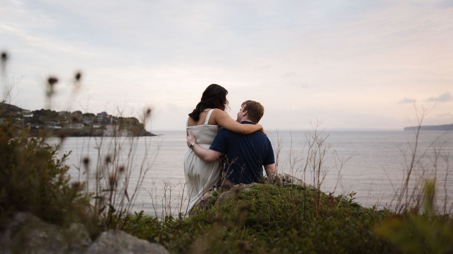 Couple embracing on coastal cliff during sunset.