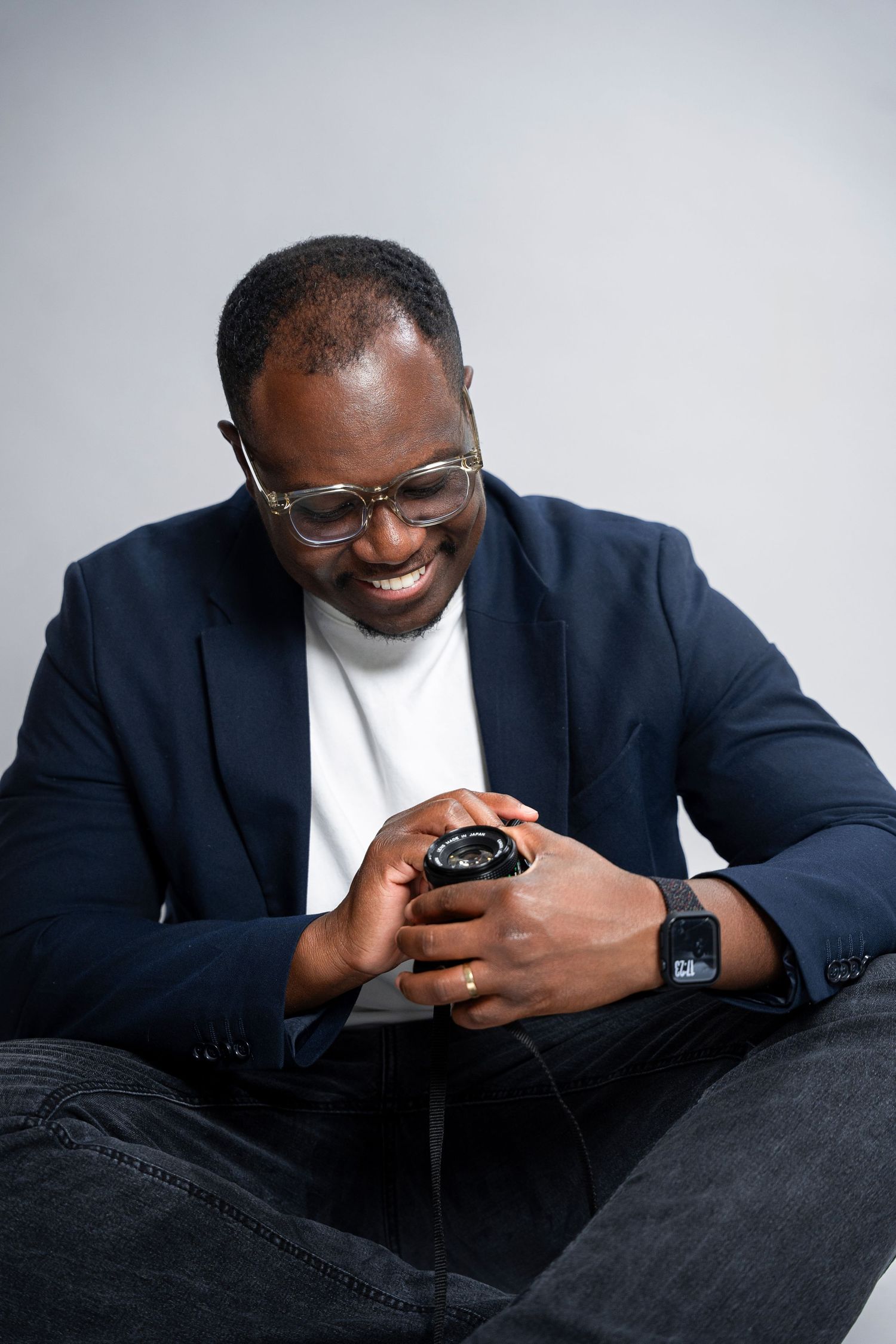 Professional wearing a navy suit and white shirt looks down at smartphone while smiling in sequence of casual poses.