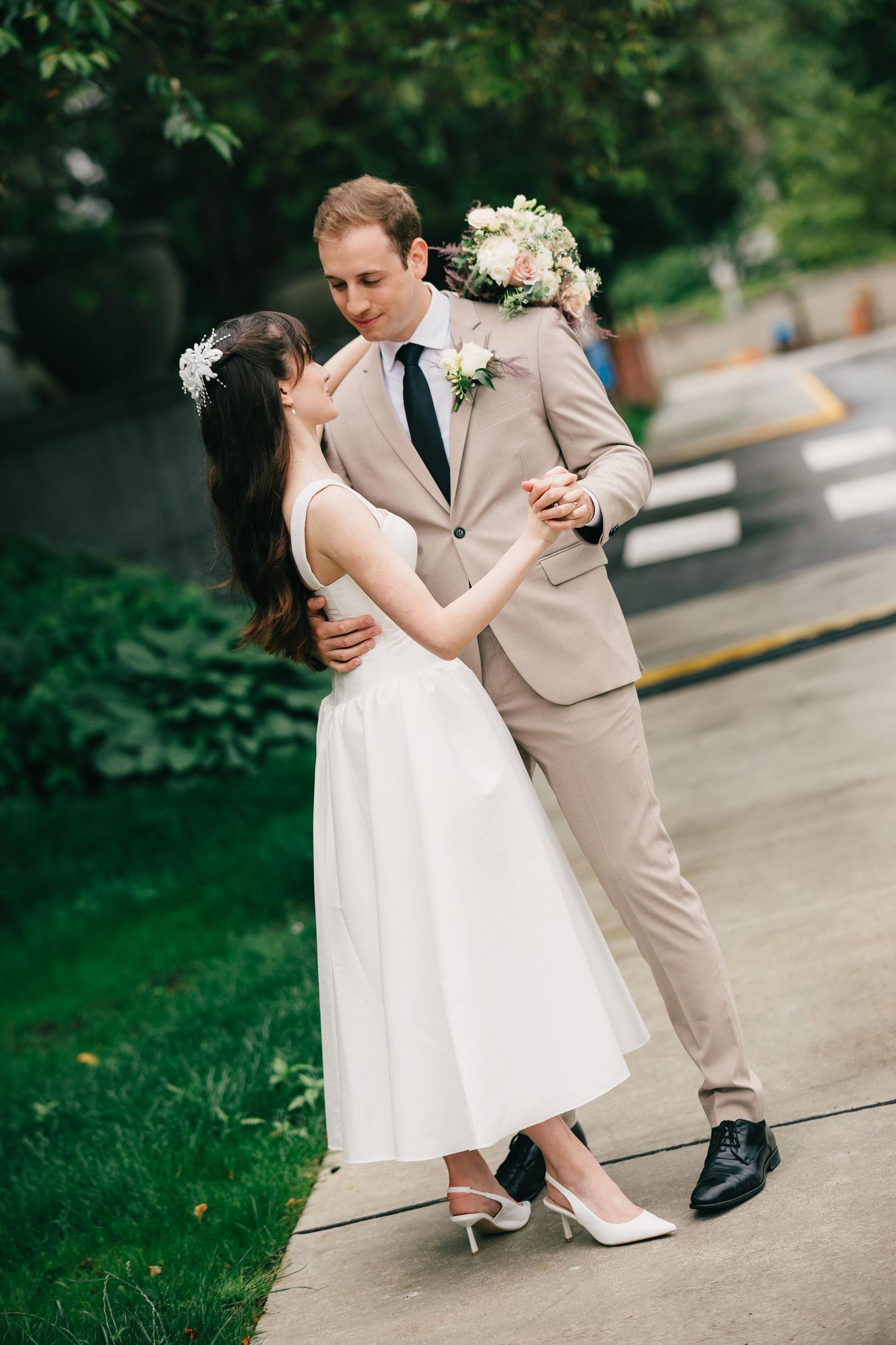 A tender moment between two people in wedding attire dancing together on a paved outdoor surface.