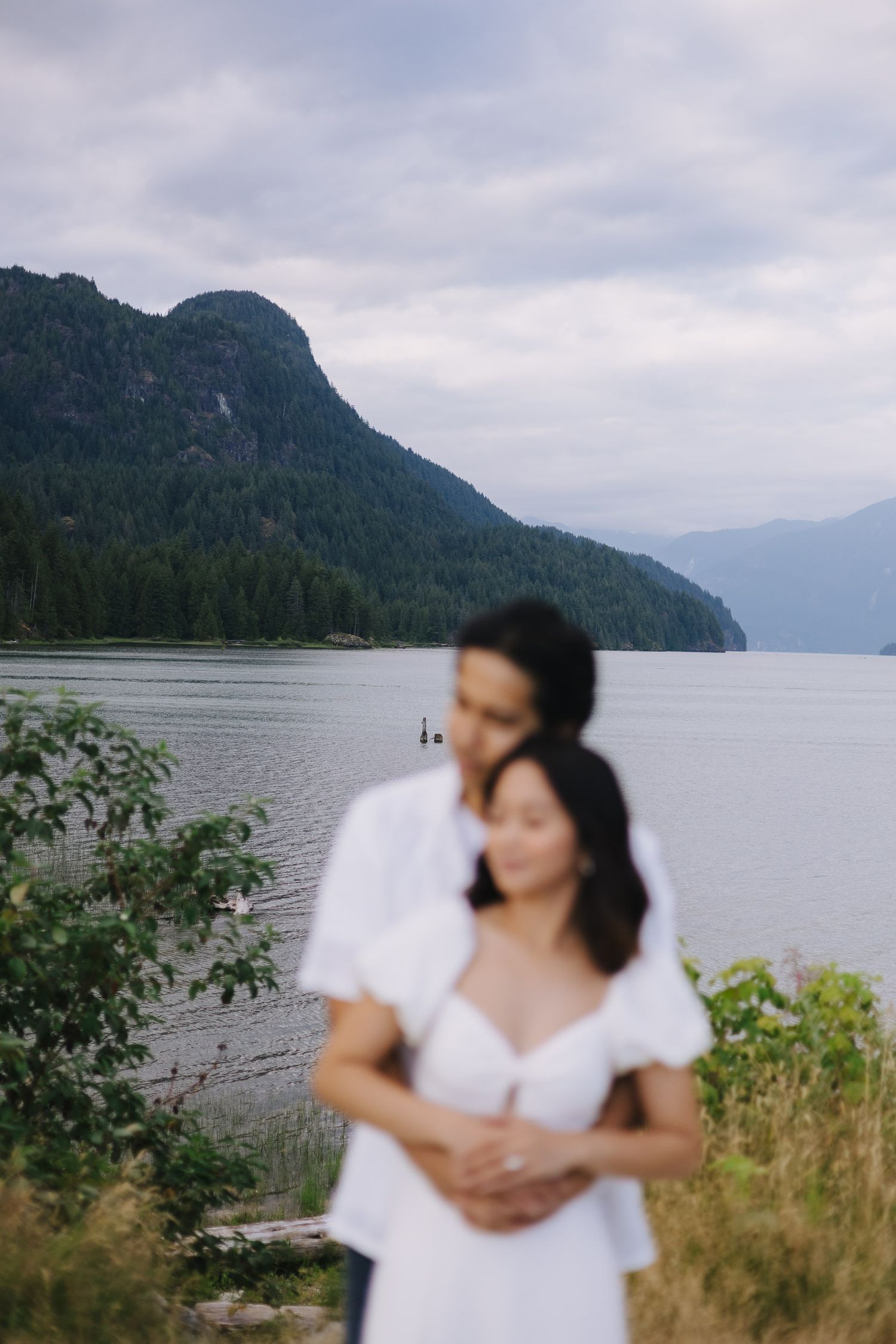 A serene mountain lake landscape with evergreen forests and cloudy skies creates a moody Pacific Northwest atmosphere.