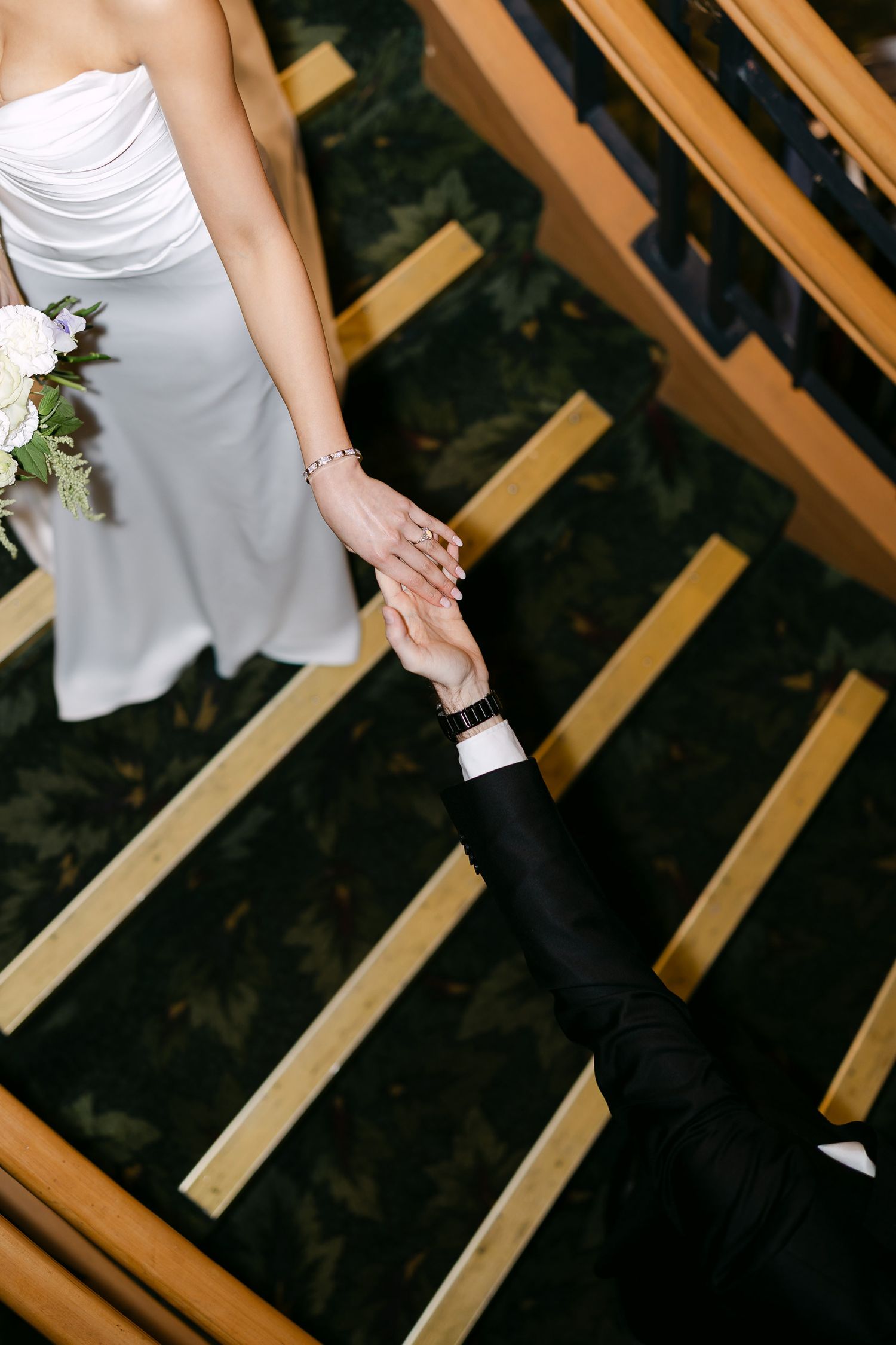 Overhead view of bride and groom holding hands on wooden staircase at wedding venue.