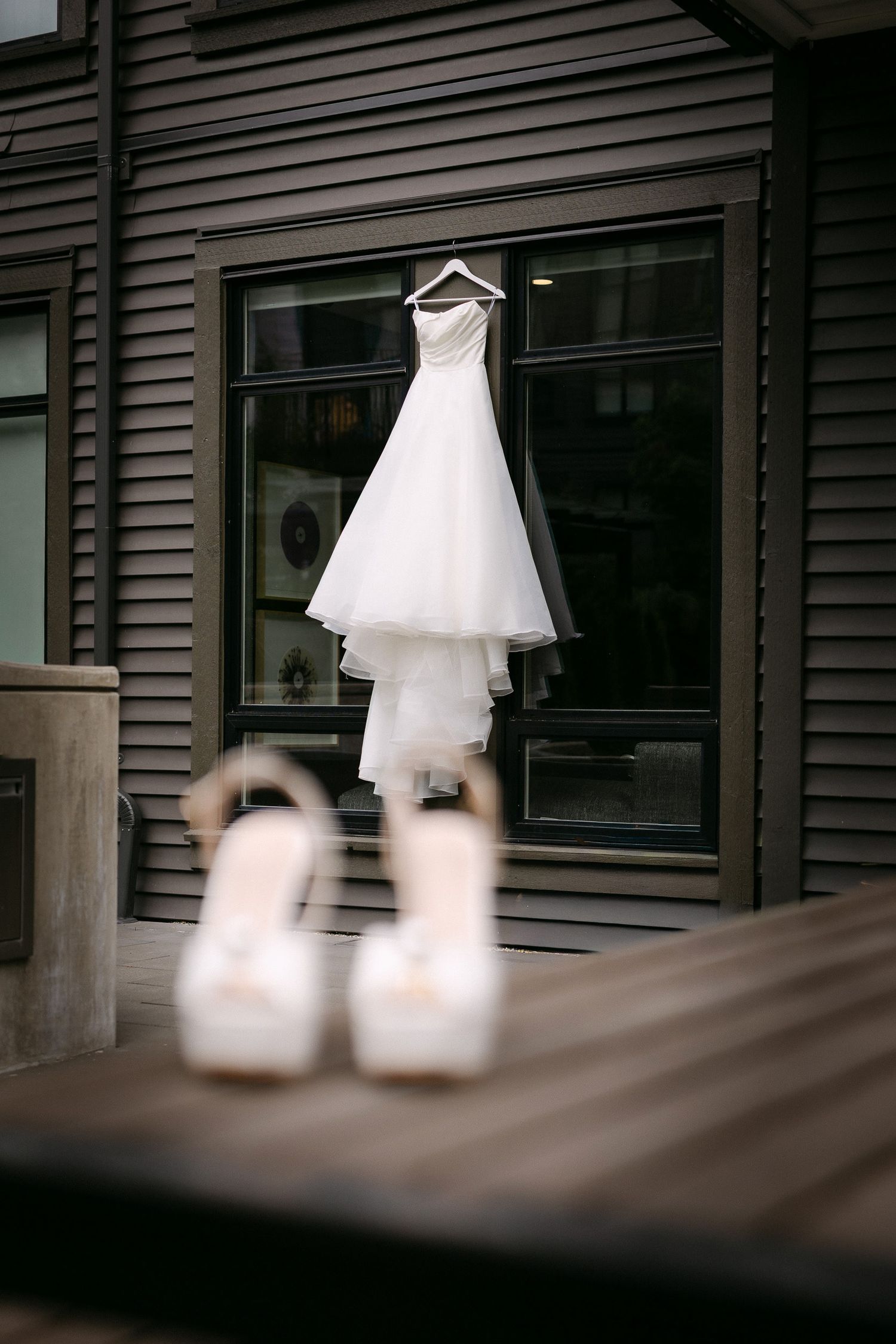 White wedding dress hanging on a window with blurred bridal heels in the foreground.