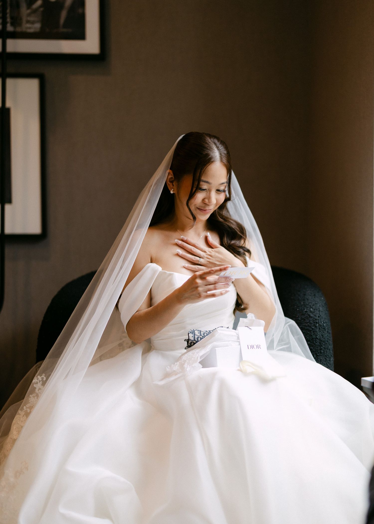A bride in a white strapless ball gown and veil sits gracefully, looking down at her hands on her wedding day.