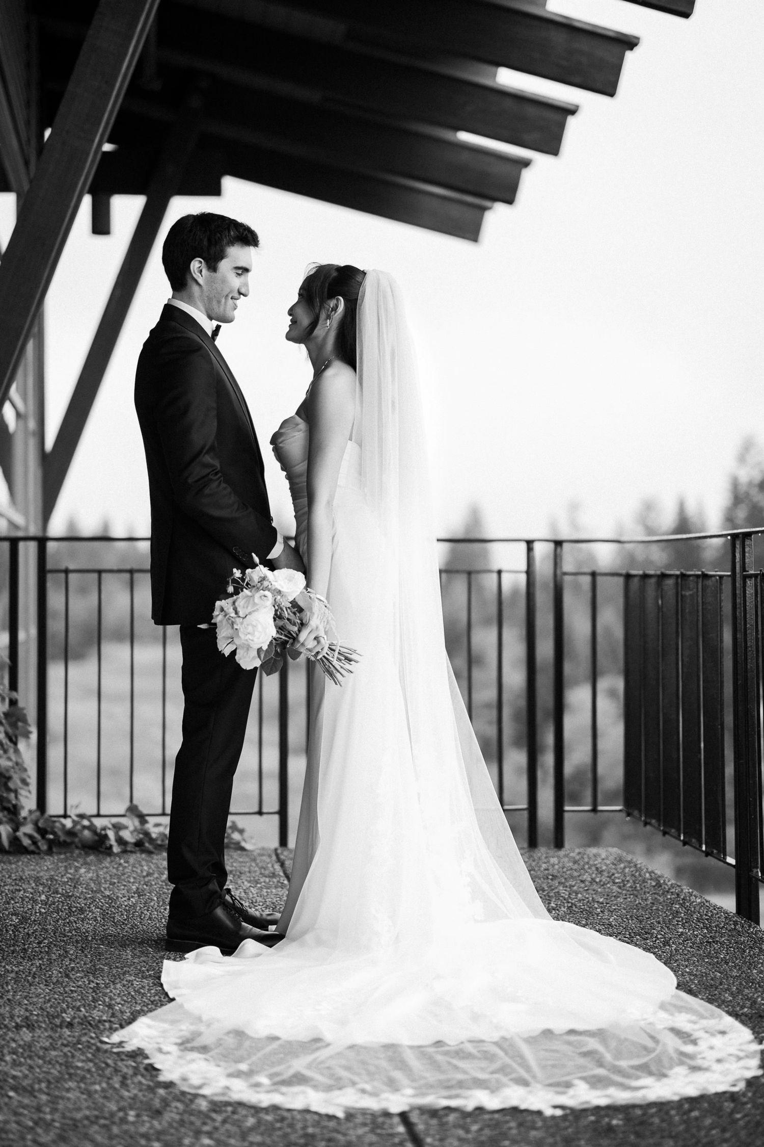Black and white photo of a bride and groom sharing an intimate moment on an outdoor terrace, bride wearing a long veil.