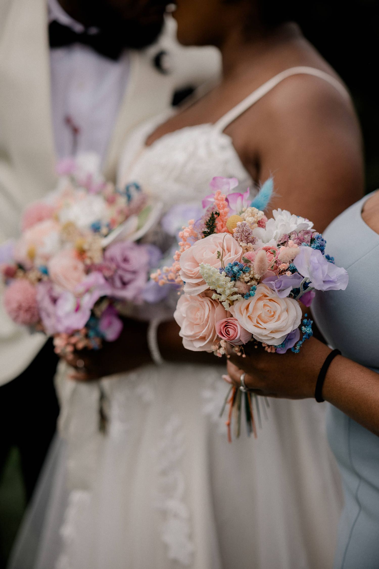 Wedding bouquets featuring soft pink roses and blue accents held by bridesmaids in white and light blue dresses.