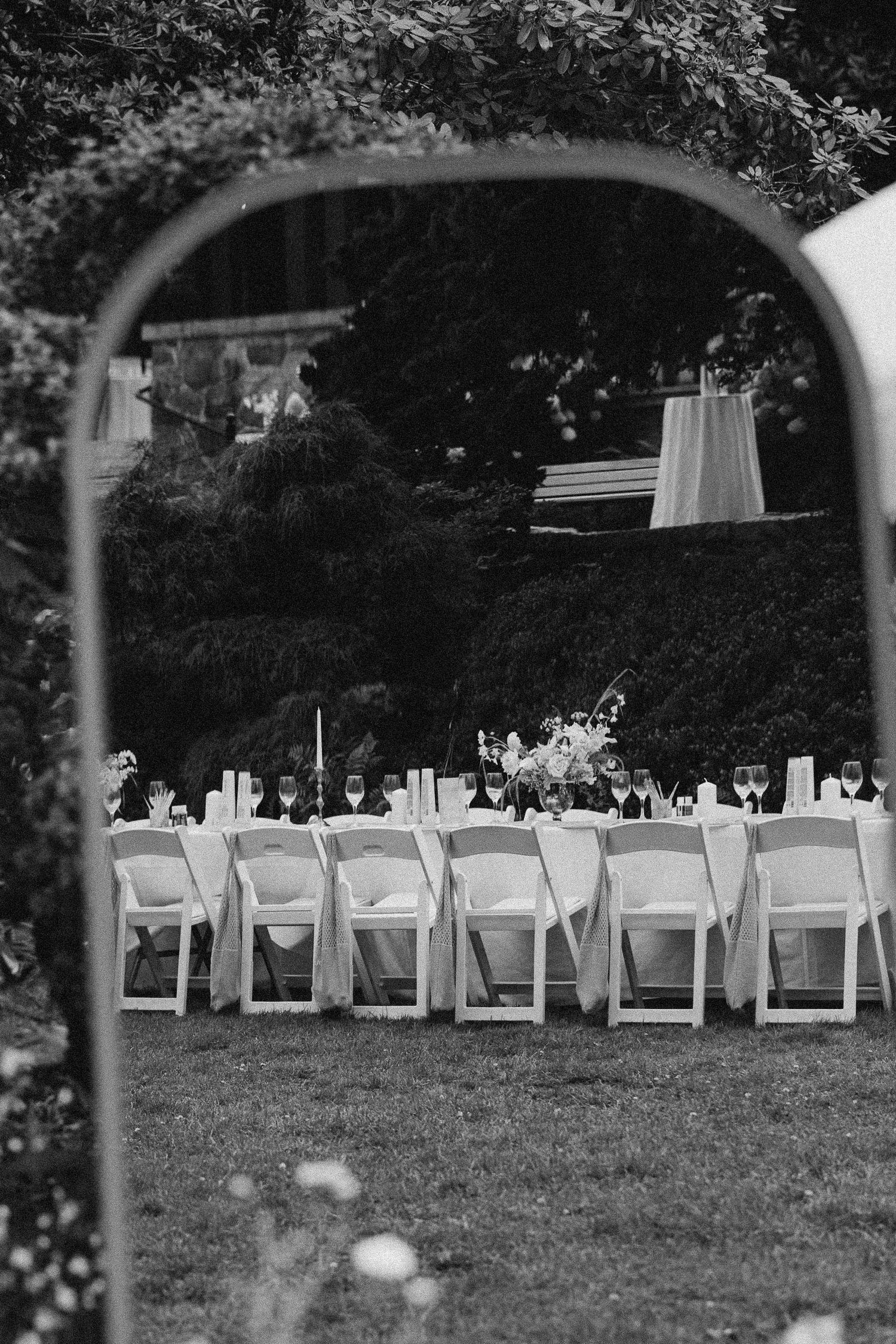 Empty white folding chairs arranged in rows on a grassy lawn for an outdoor wedding ceremony.