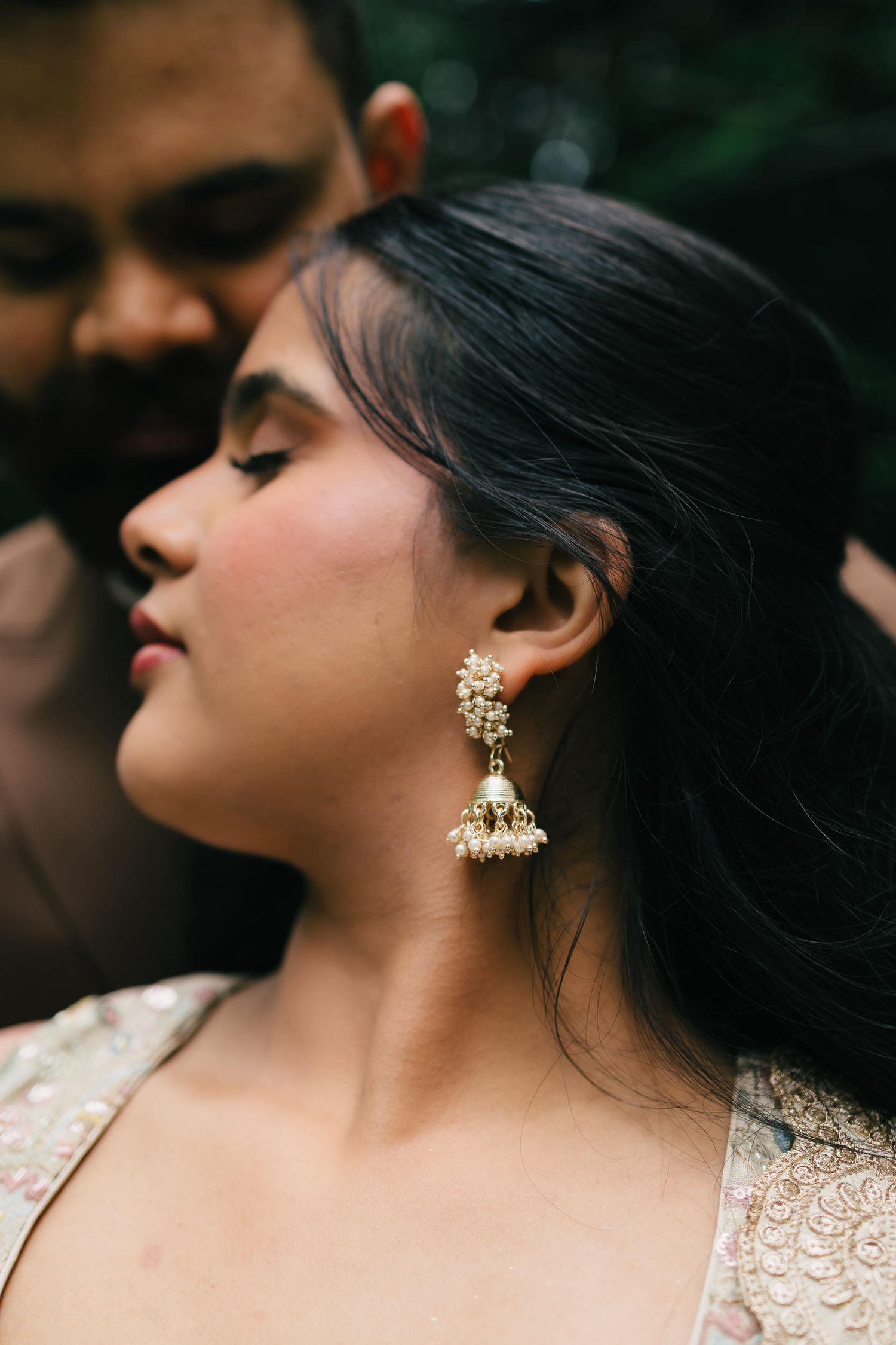 Close up profile view of an elegant ornate gold chandelier earring against dark hair and lace dress.