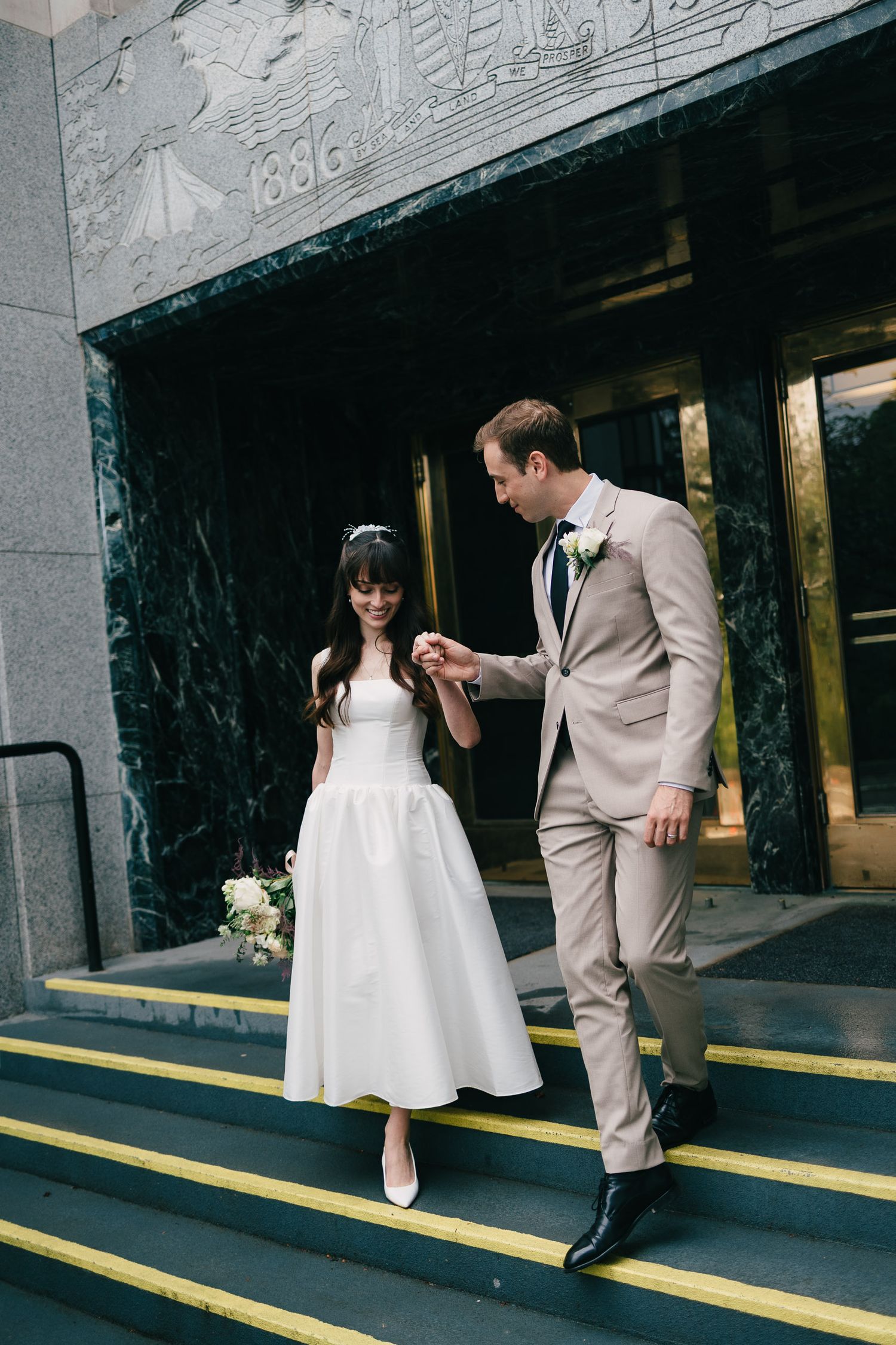 A couple in wedding attire shares a playful moment at a subway platform with marble walls.
