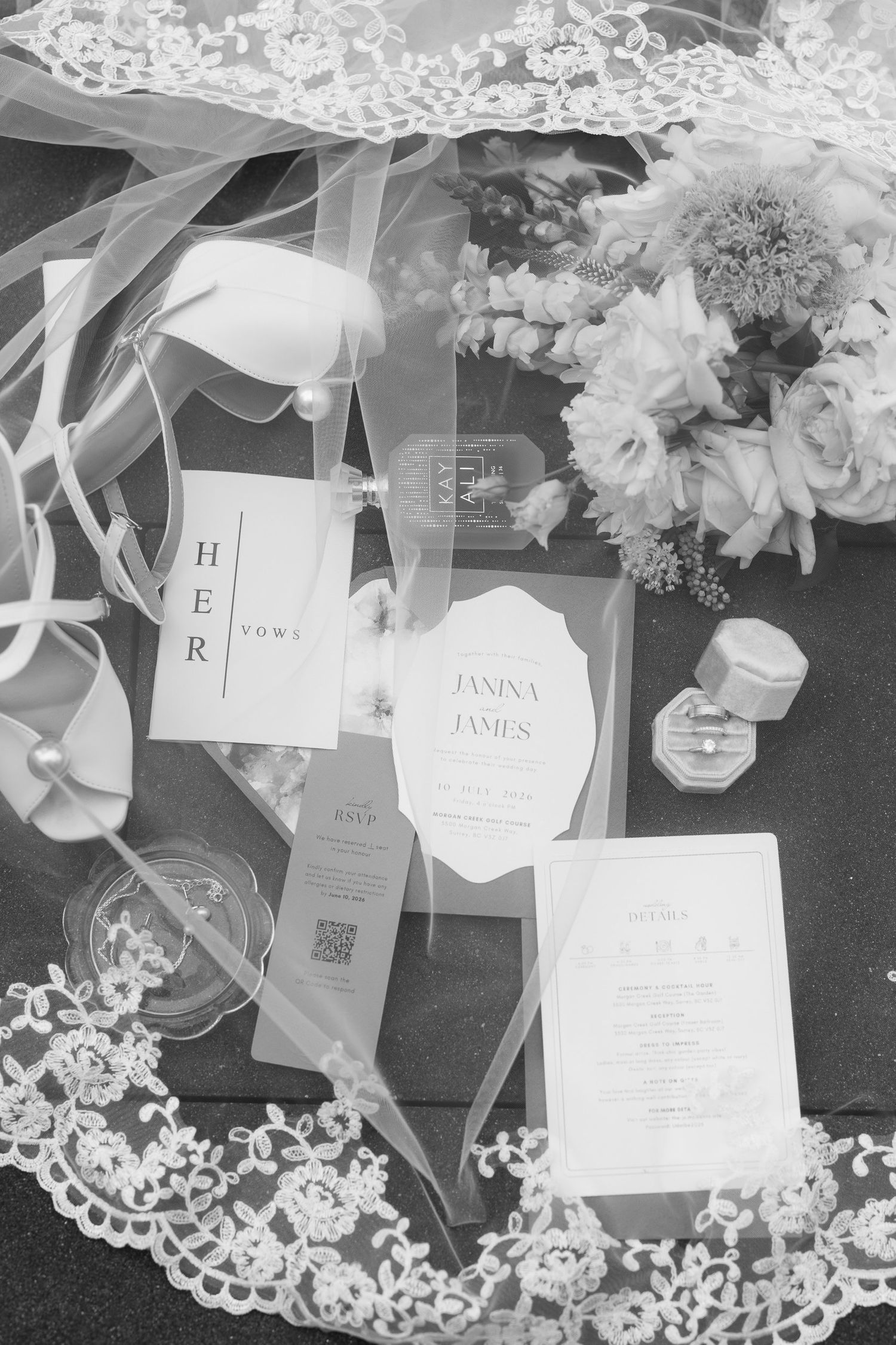 Black and white flat lay of wedding stationery, bridal veil, perfume, and floral bouquet for Janina and James.