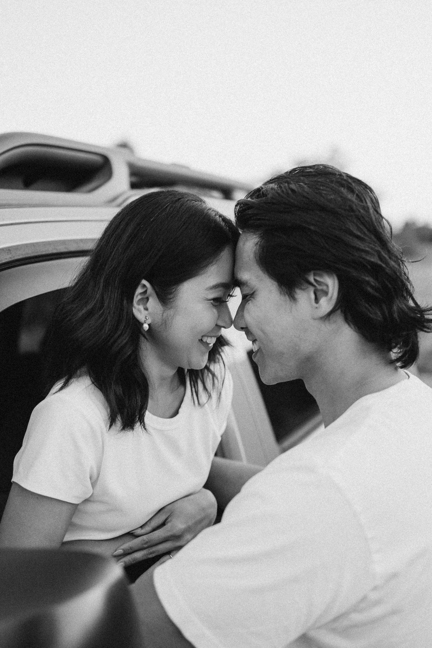 A couple shares intimate moments in black and white while leaning against a car.