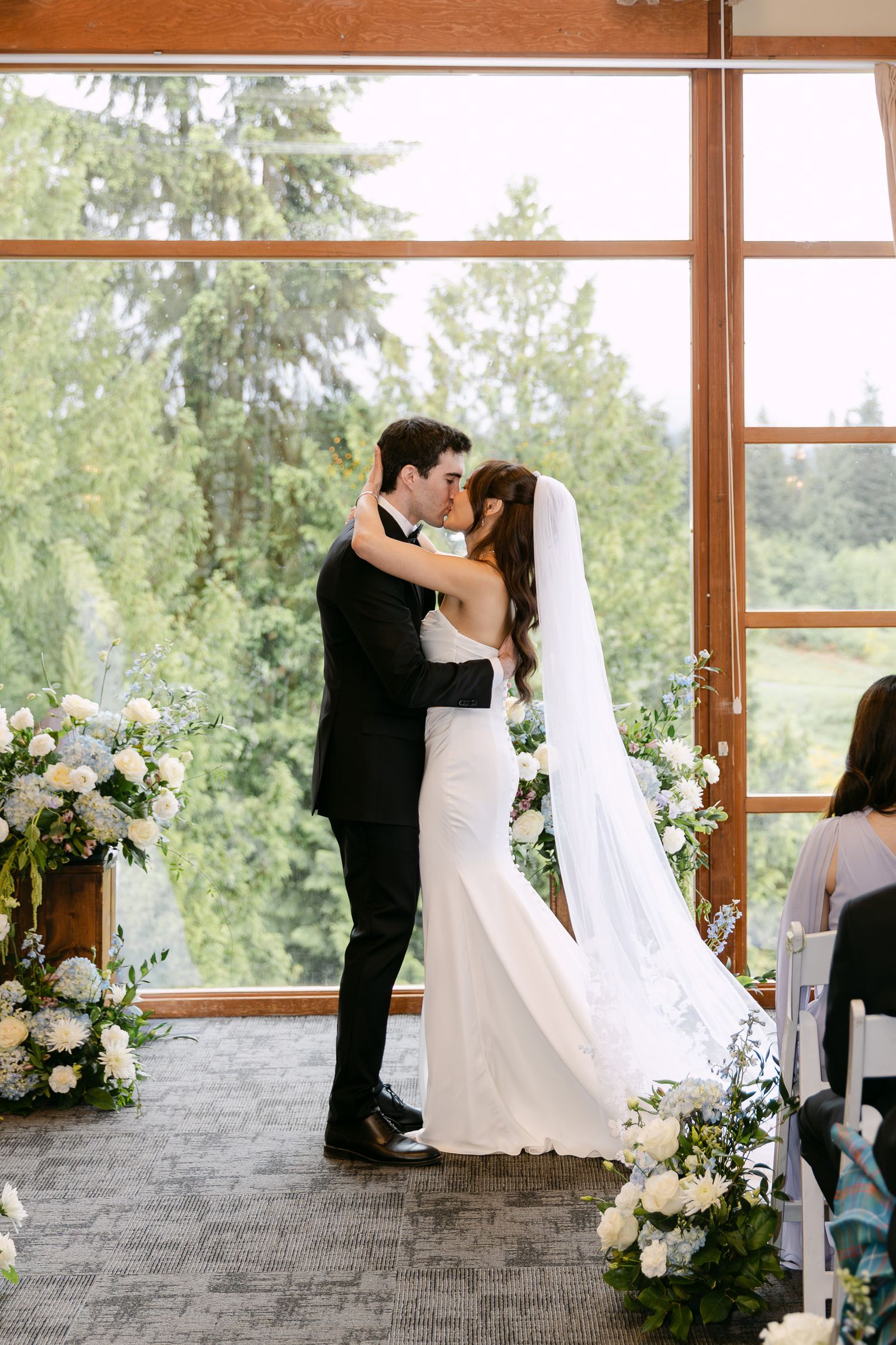 Bride and groom share first kiss at altar with lush garden views and white floral decor.