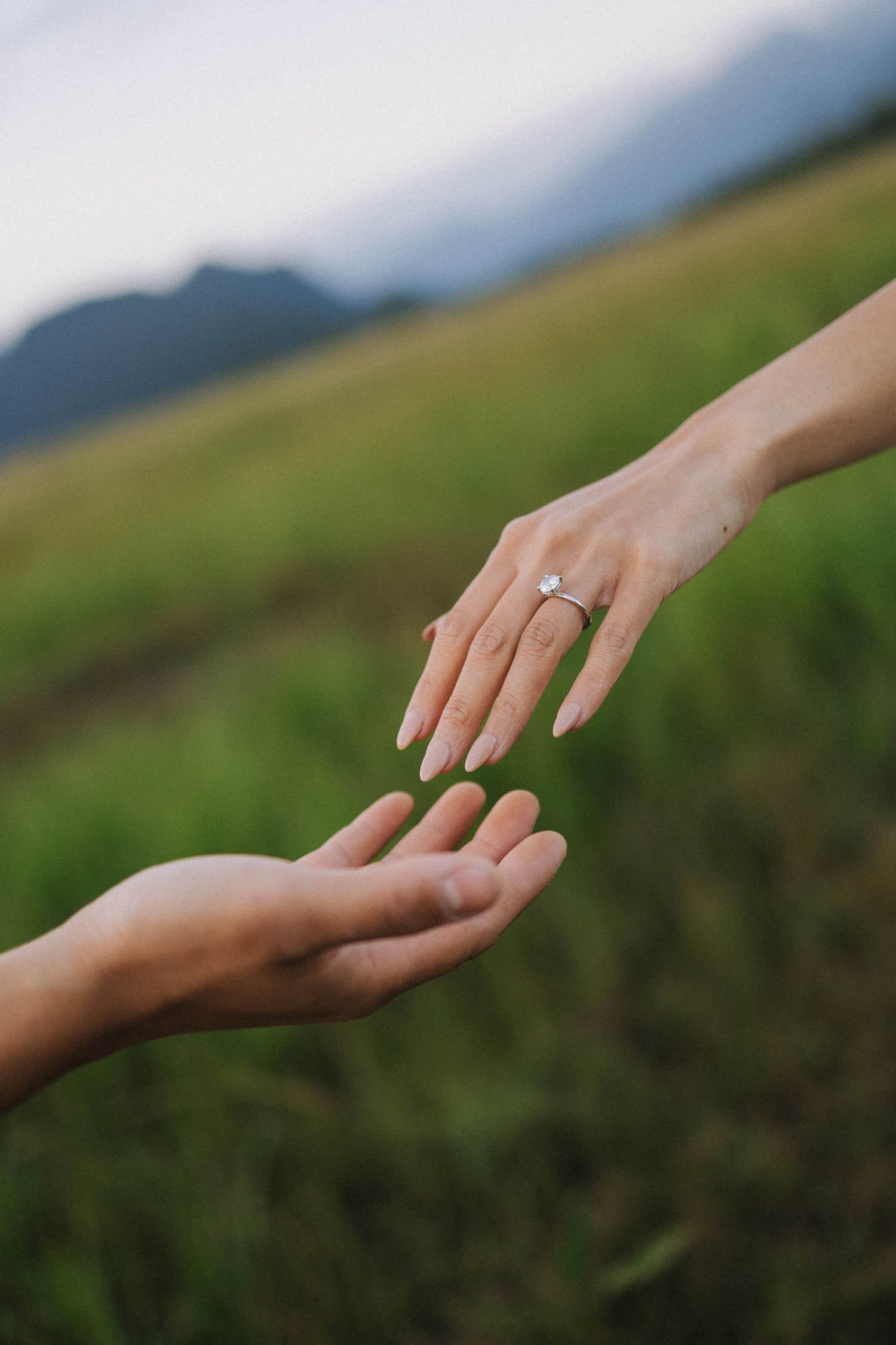 Close-up shot of hands reaching towards each other against a blurred green mountain landscape background.