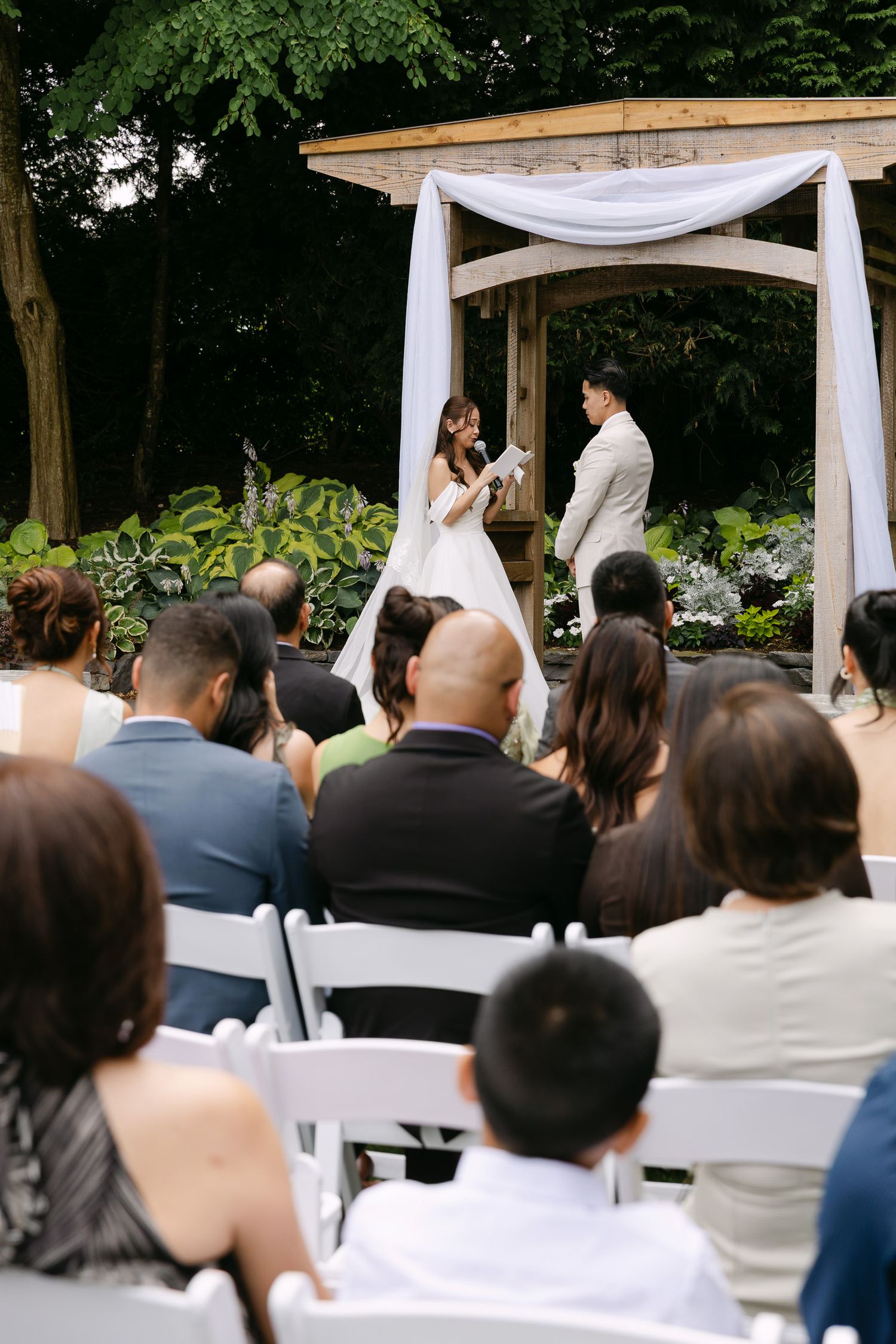 Wedding ceremony with bride and groom at floral arch before seated guests in garden.