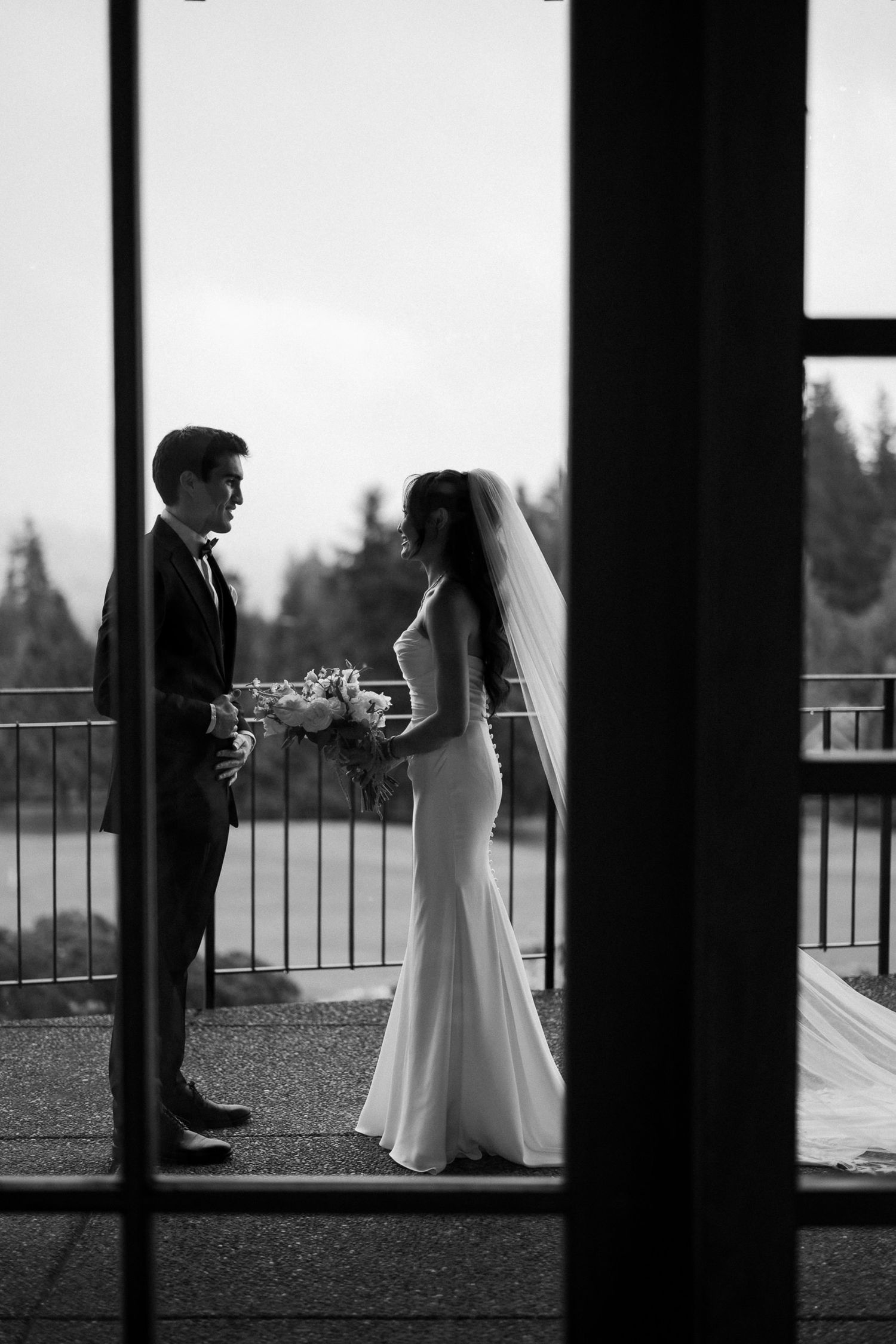 Black and white photo of bride and groom sharing a romantic first look moment on an outdoor balcony.