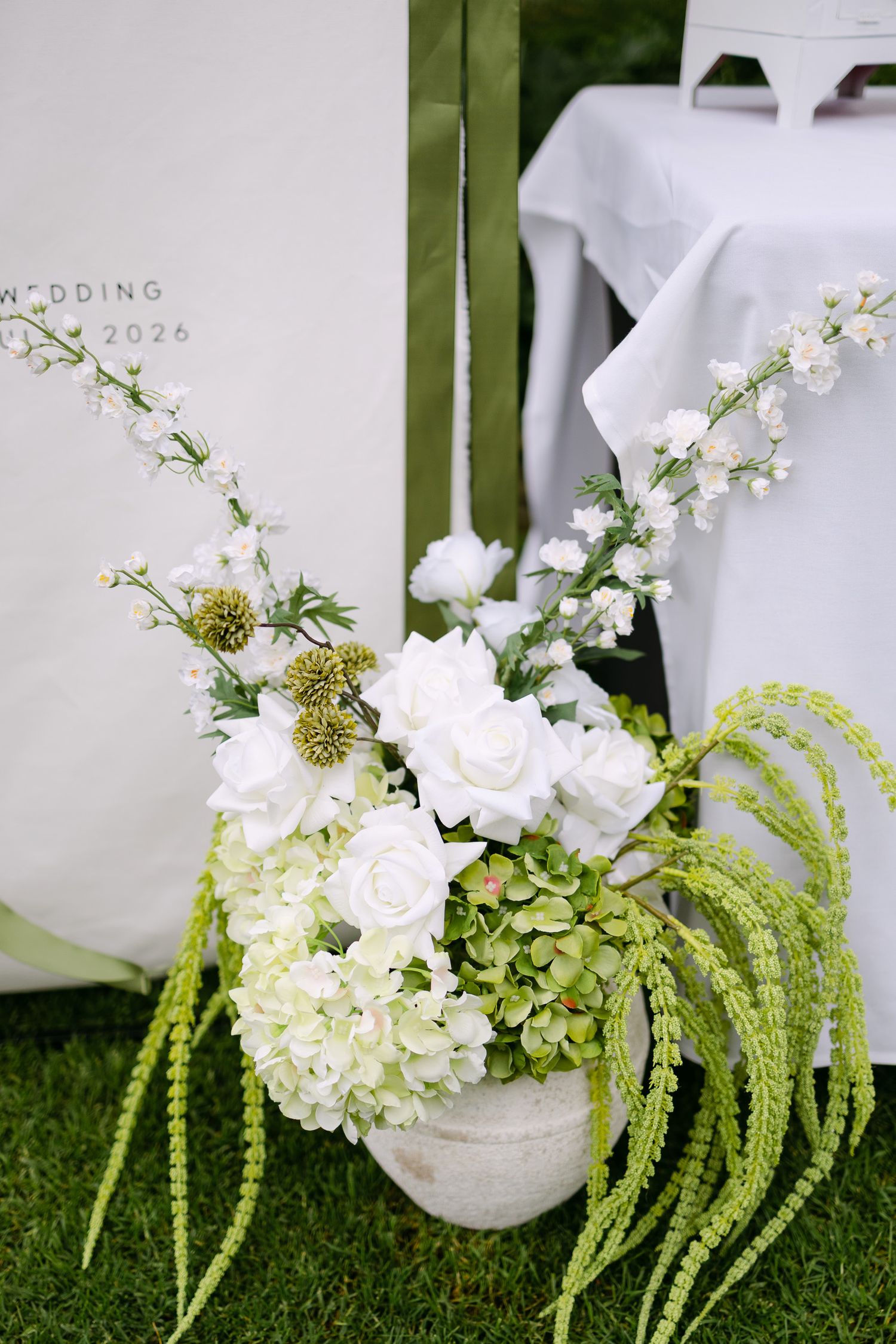 Elegant wedding floral arrangement with white roses, hydrangeas, and green accents in a stone pot, 2026 wedding backdrop.