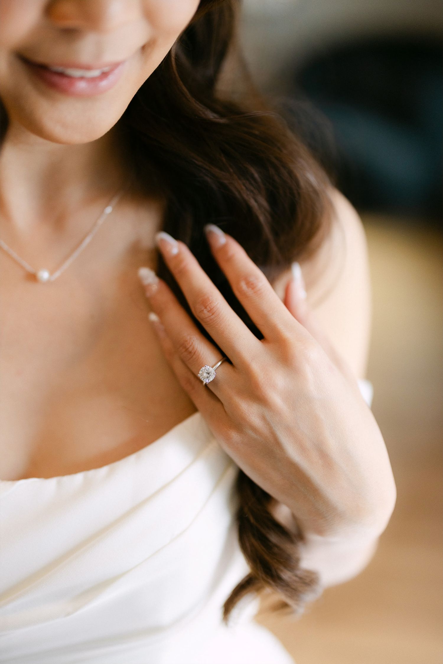 Bride showcasing a stunning cushion-cut diamond engagement ring on her hand while wearing a white strapless wedding gown.