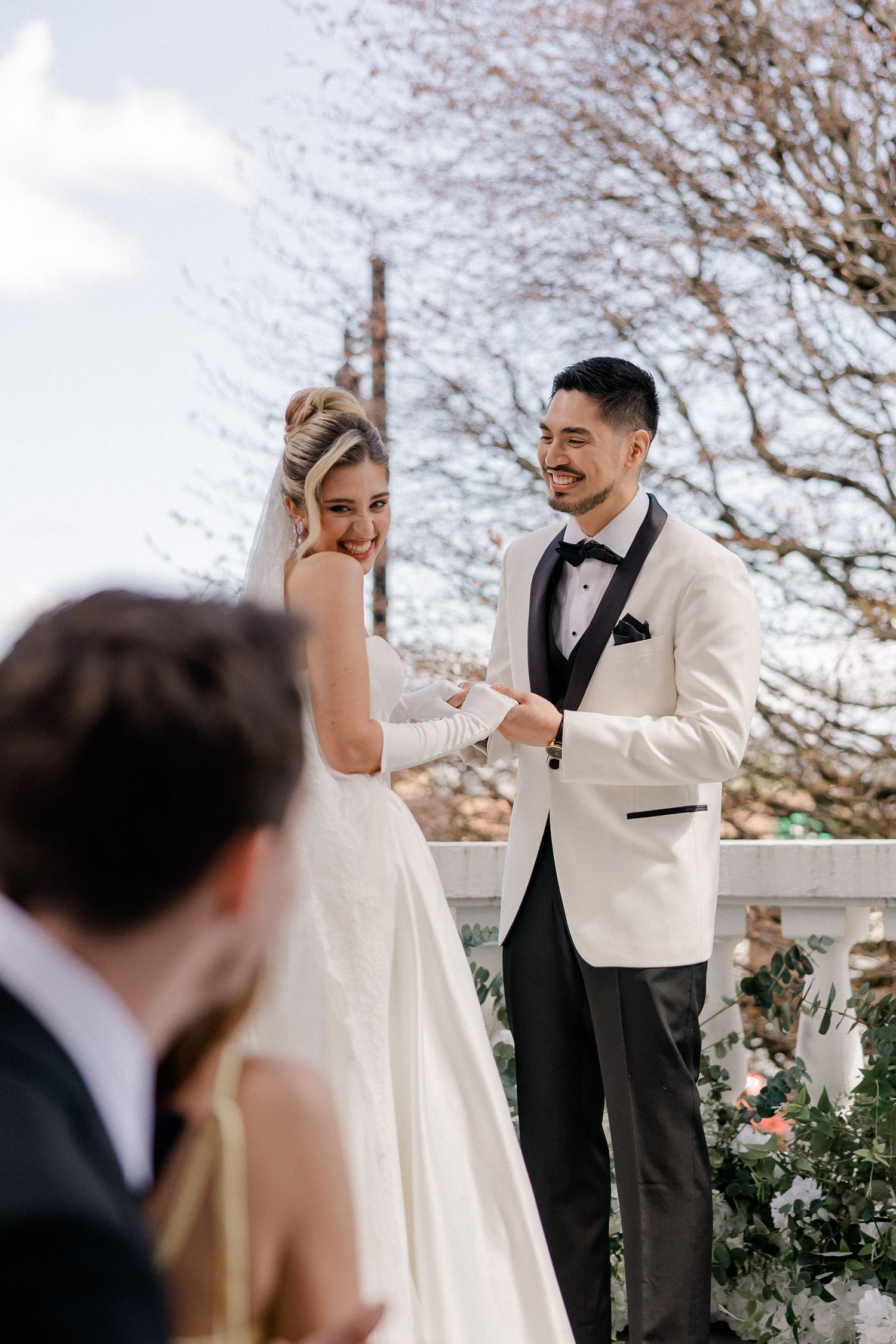 A couple shares a joyful moment during their wedding ceremony while wearing elegant white and black formal attire.