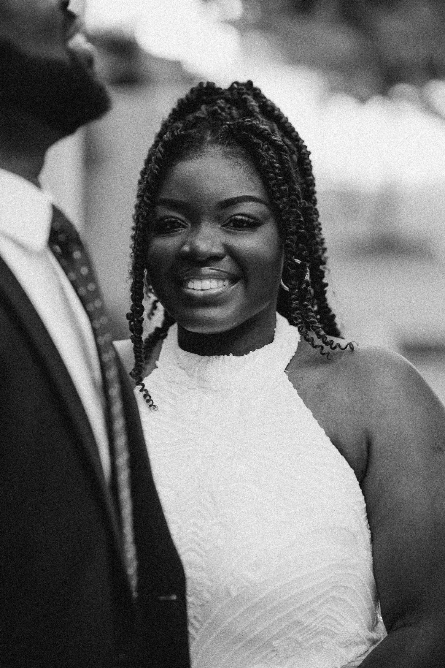 A joyful bride in a sleeveless white lace dress smiles radiantly in a series of black and white wedding portraits.