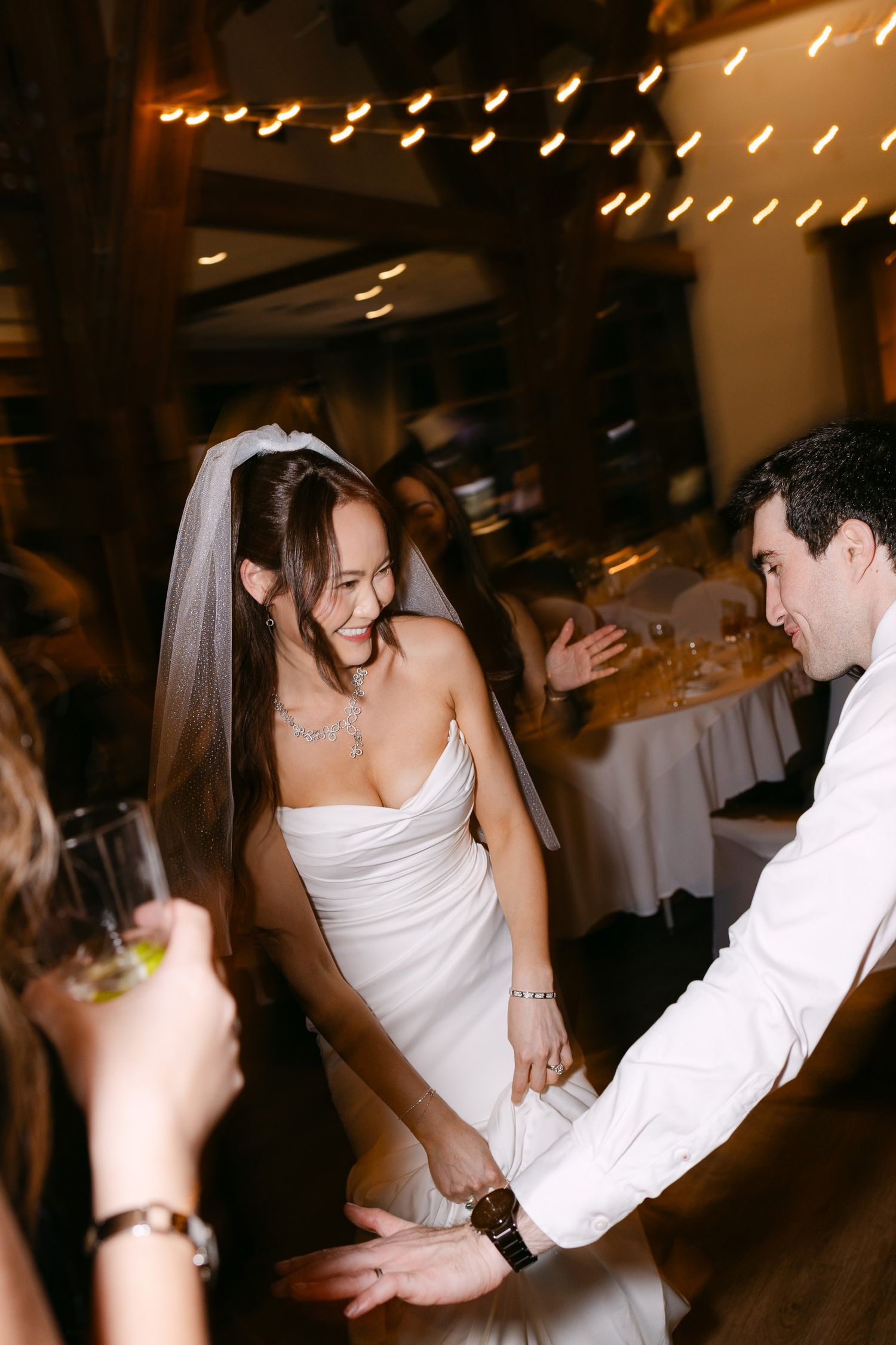 Smiling bride in white gown and veil dancing with groom at elegant wedding reception.