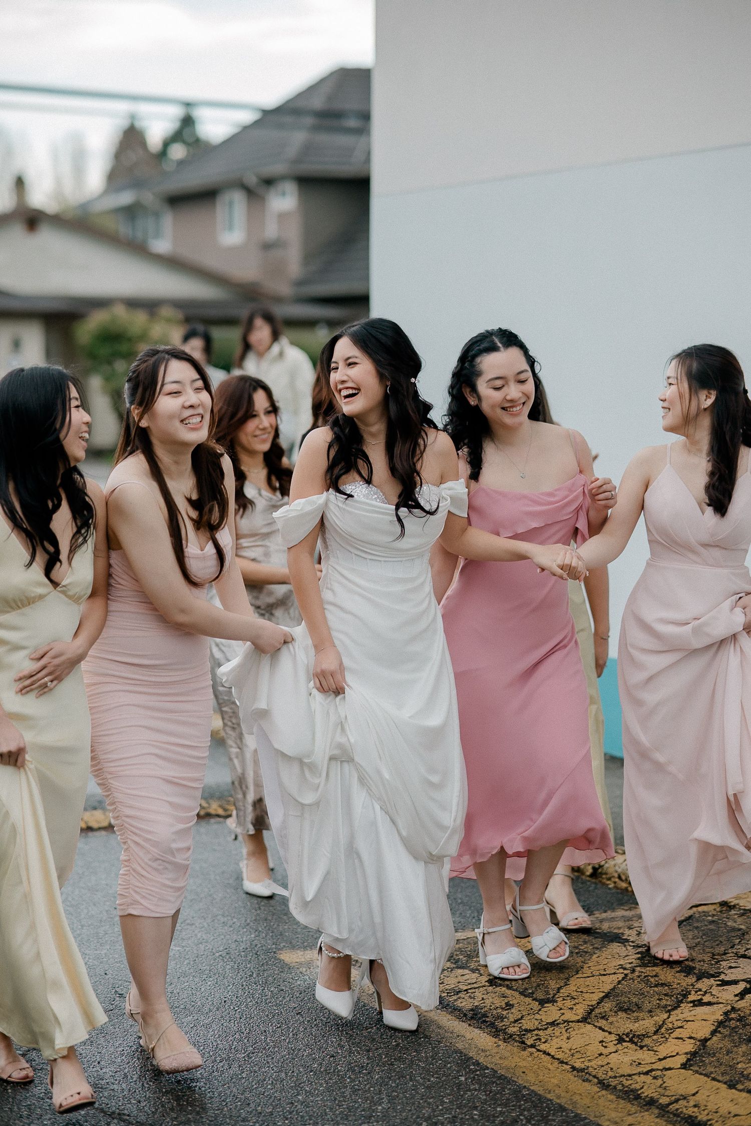 A group of bridesmaids in pink and white dresses laugh and dance together during a wedding celebration.