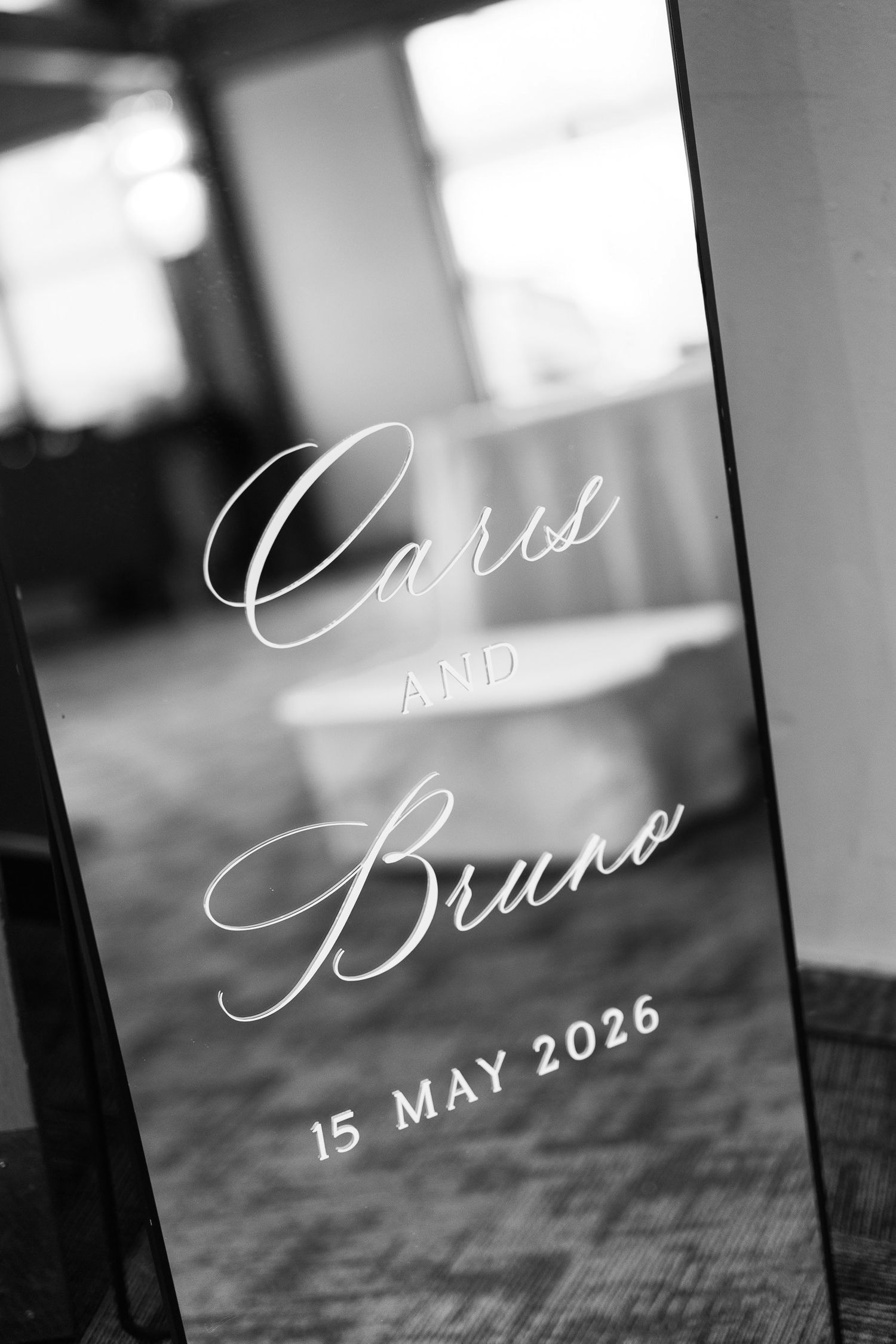 Black and white wedding mirror sign with elegant script reading Caris and Bruno, 15 May 2026.