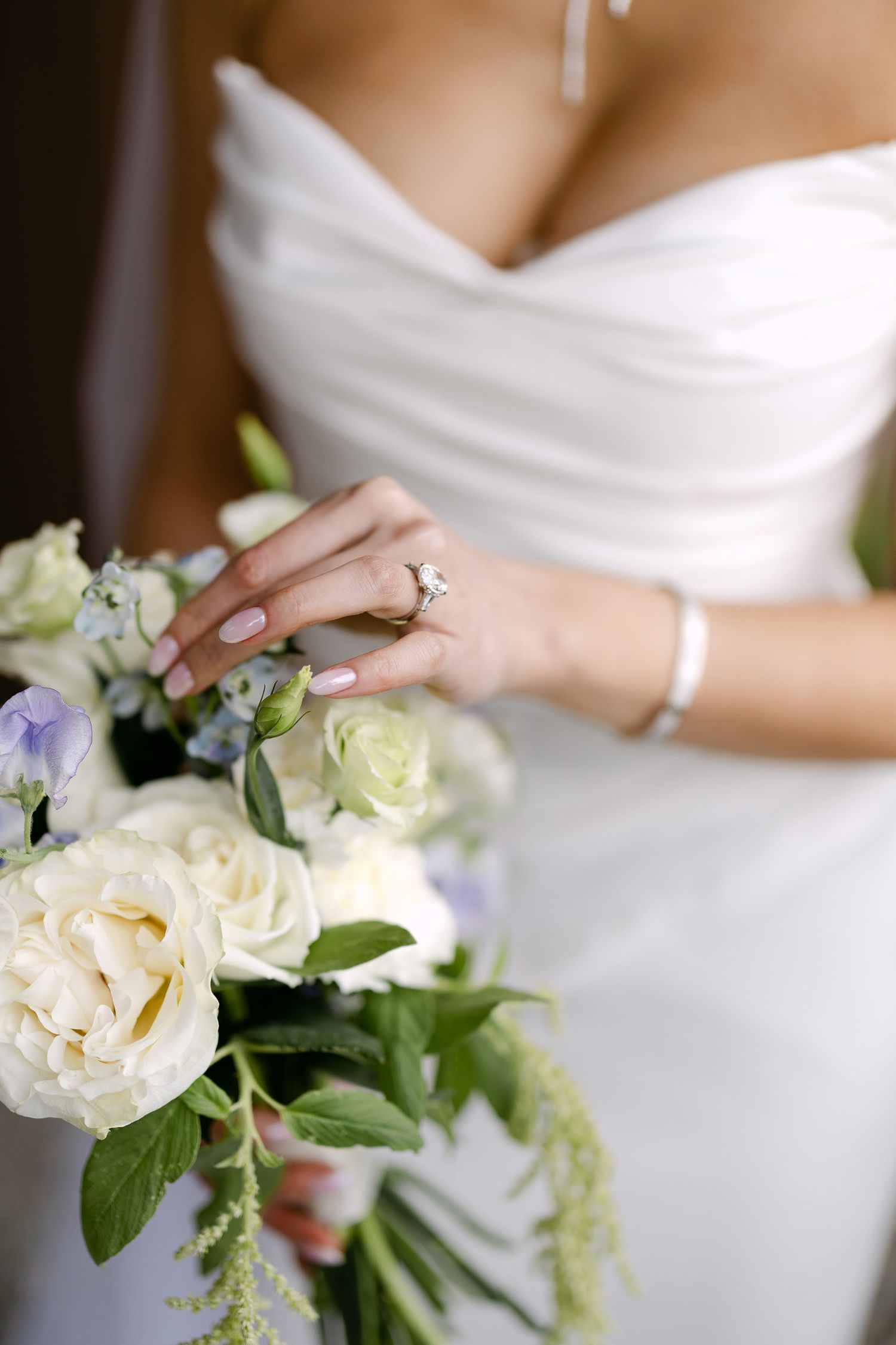 Close-up of bride's hand with diamond ring resting on white and blue floral bouquet.