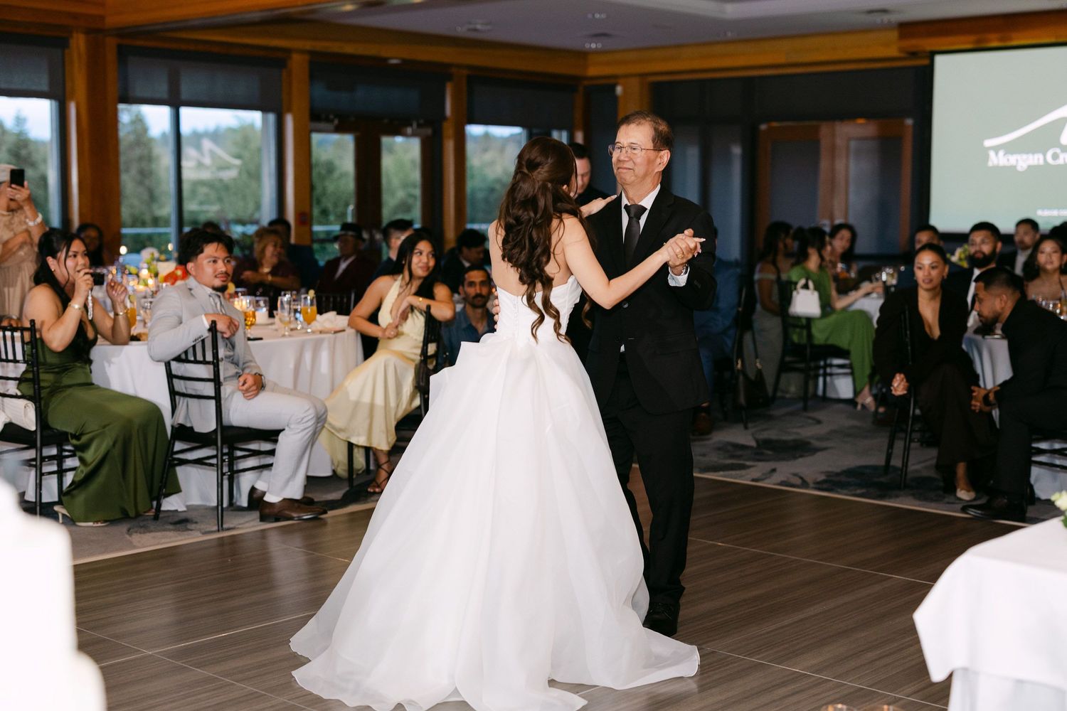 Bride in white ballgown shares first dance with father at elegant wedding reception venue.