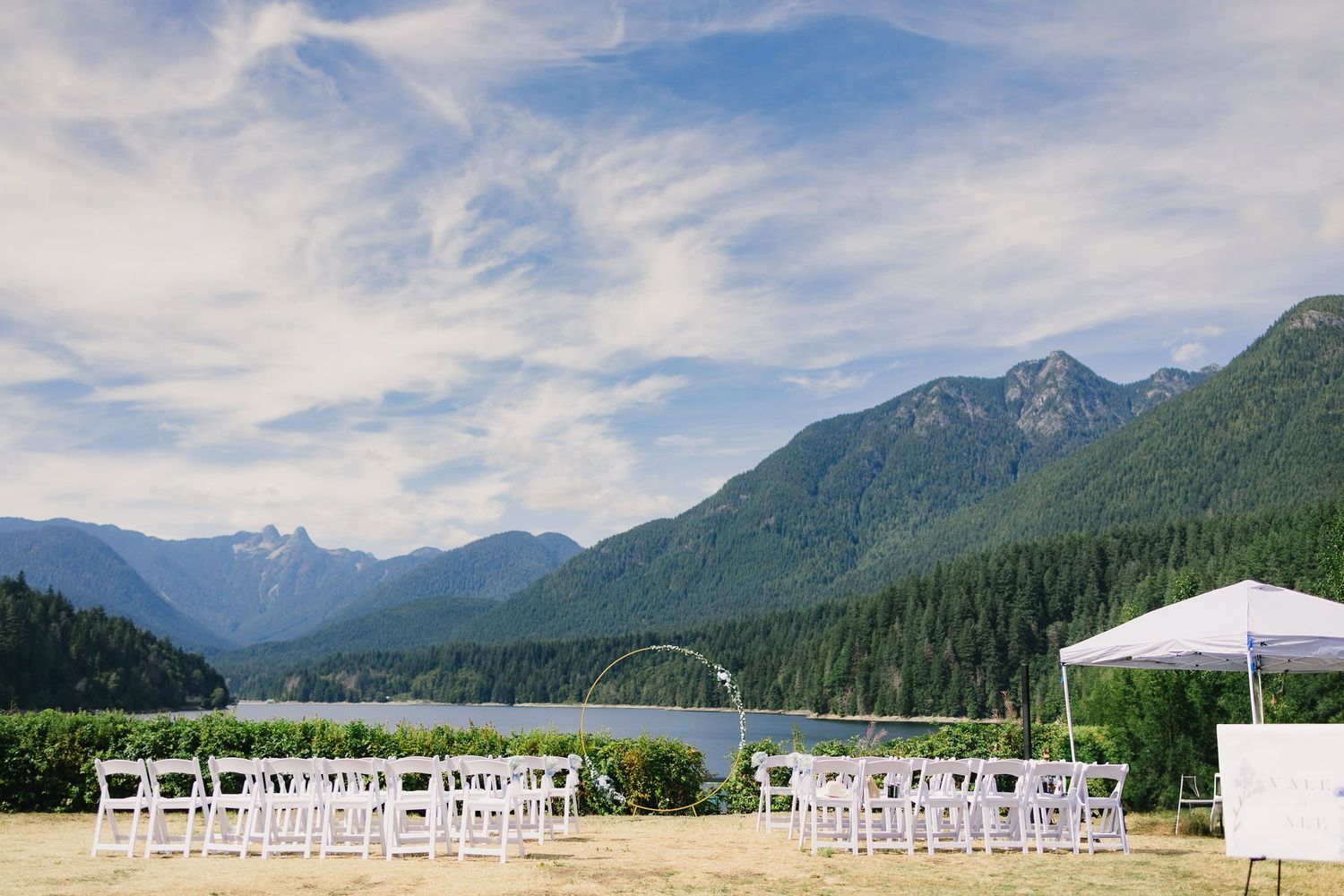 Mountain landscape panorama with white wedding chairs set up for outdoor ceremony against dramatic cloudy sky.