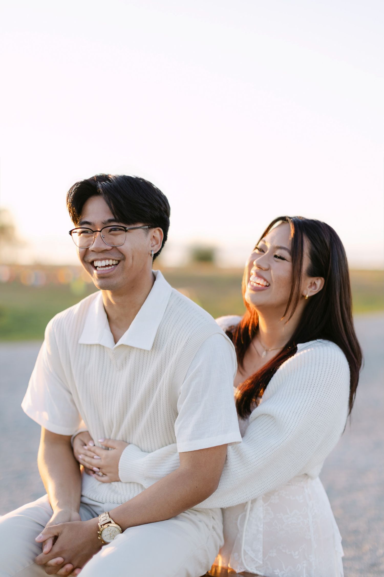 Smiling couple in cream outfits laughing together during a golden hour engagement photo session outdoors.