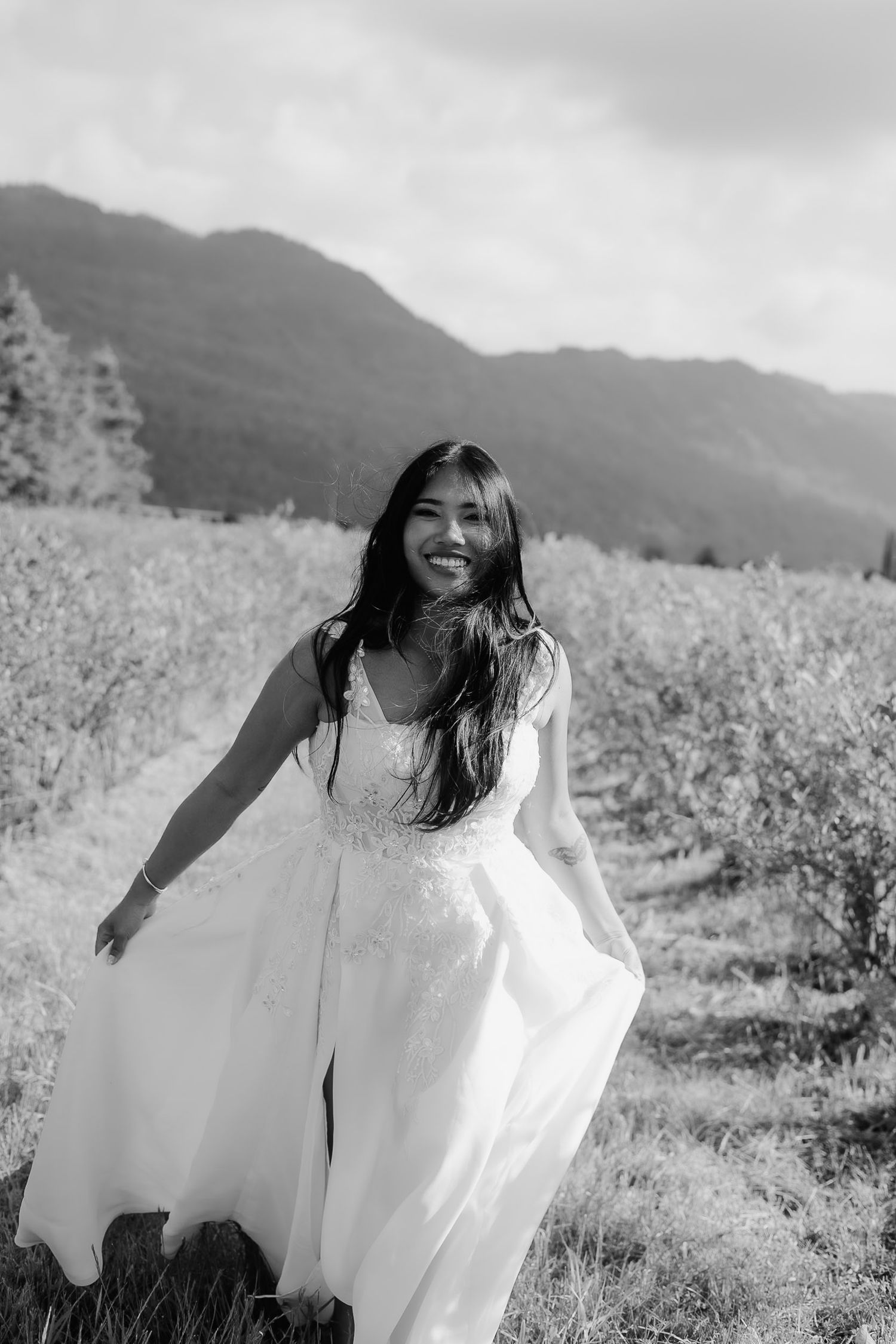 A person in a flowing white dress spins joyfully in a mountain meadow on a cloudy day.