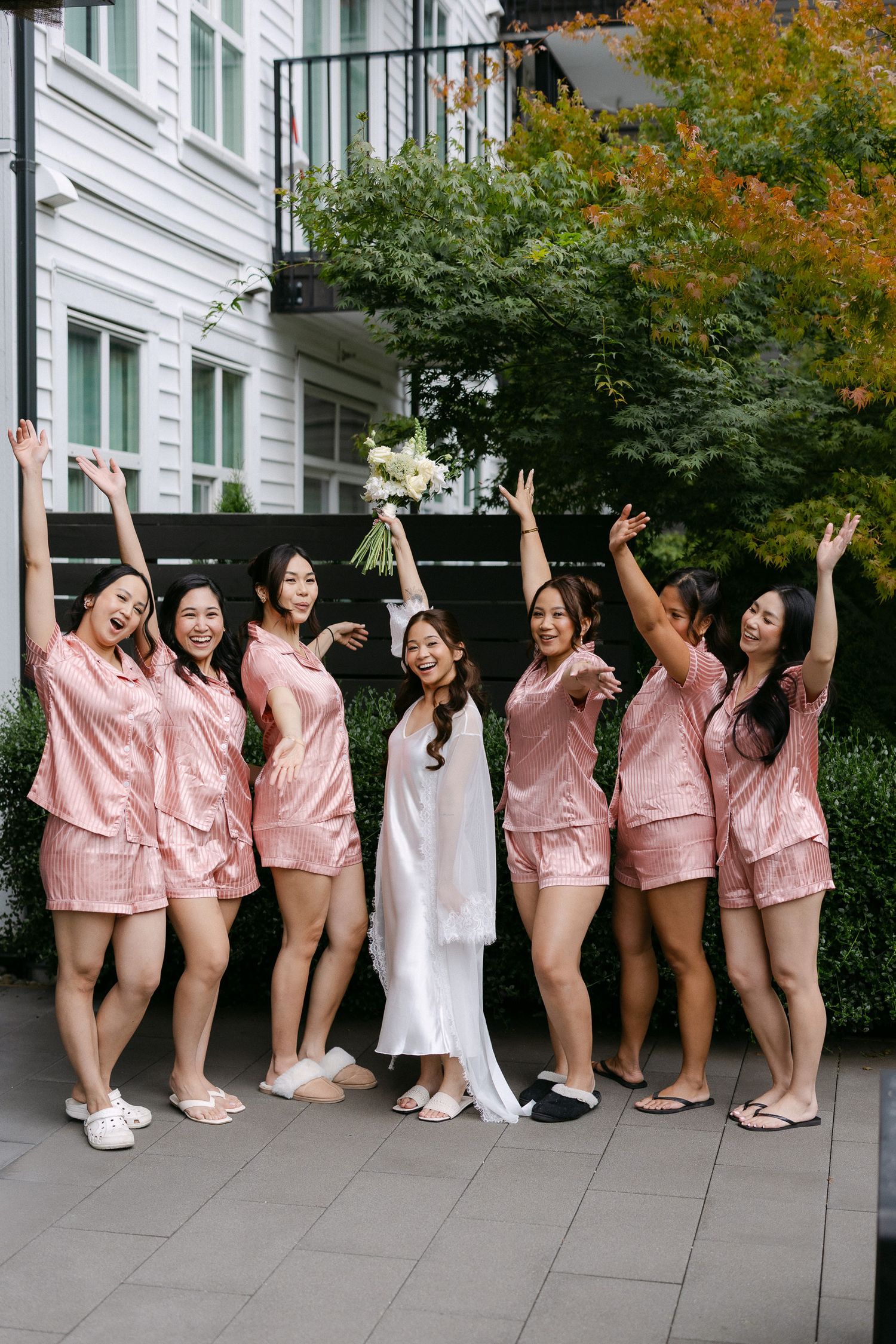 Bride with six bridesmaids in matching pink satin pajamas celebrating outdoors.