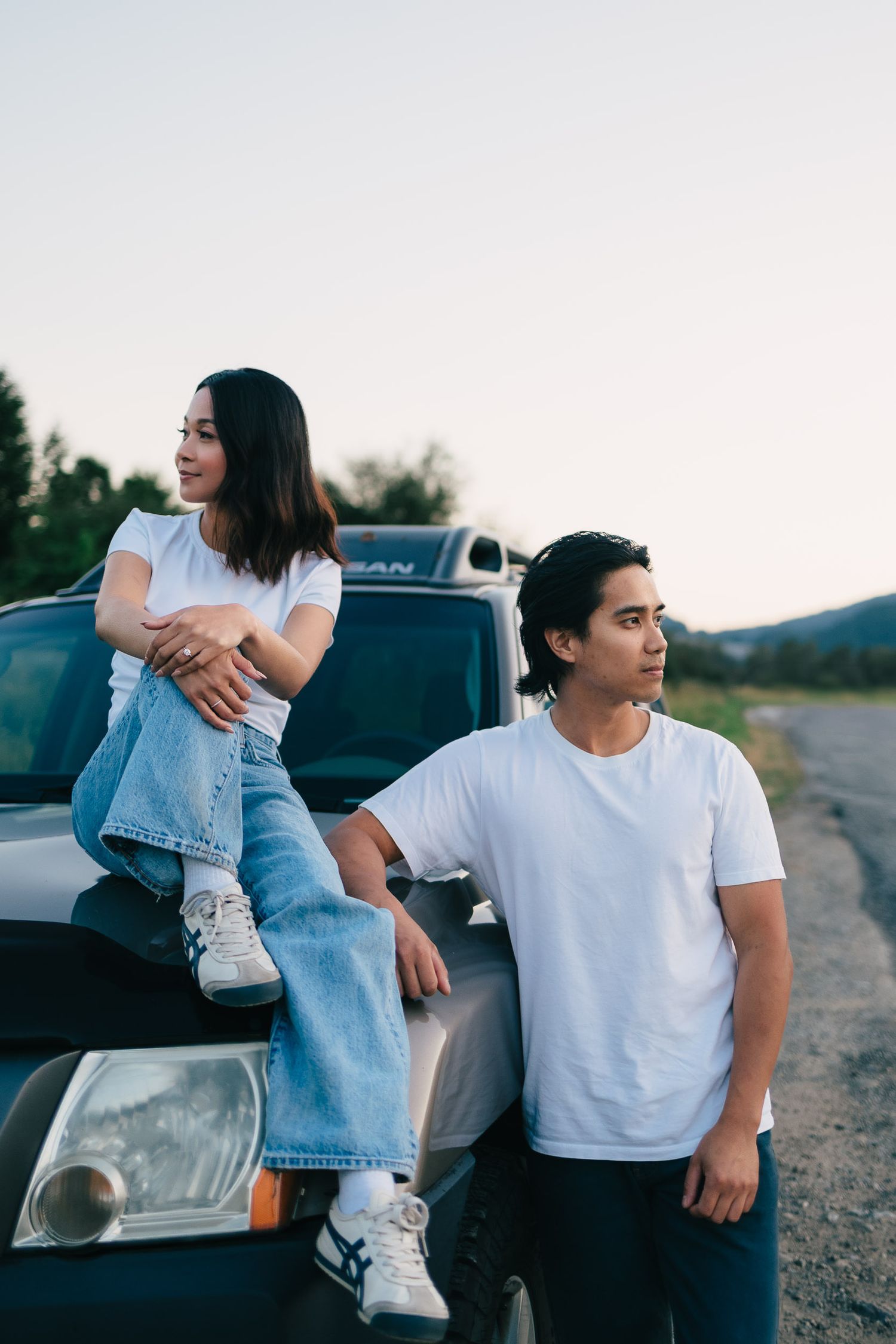 Two people in casual attire leaning against a parked pickup truck on a dirt road at dusk.