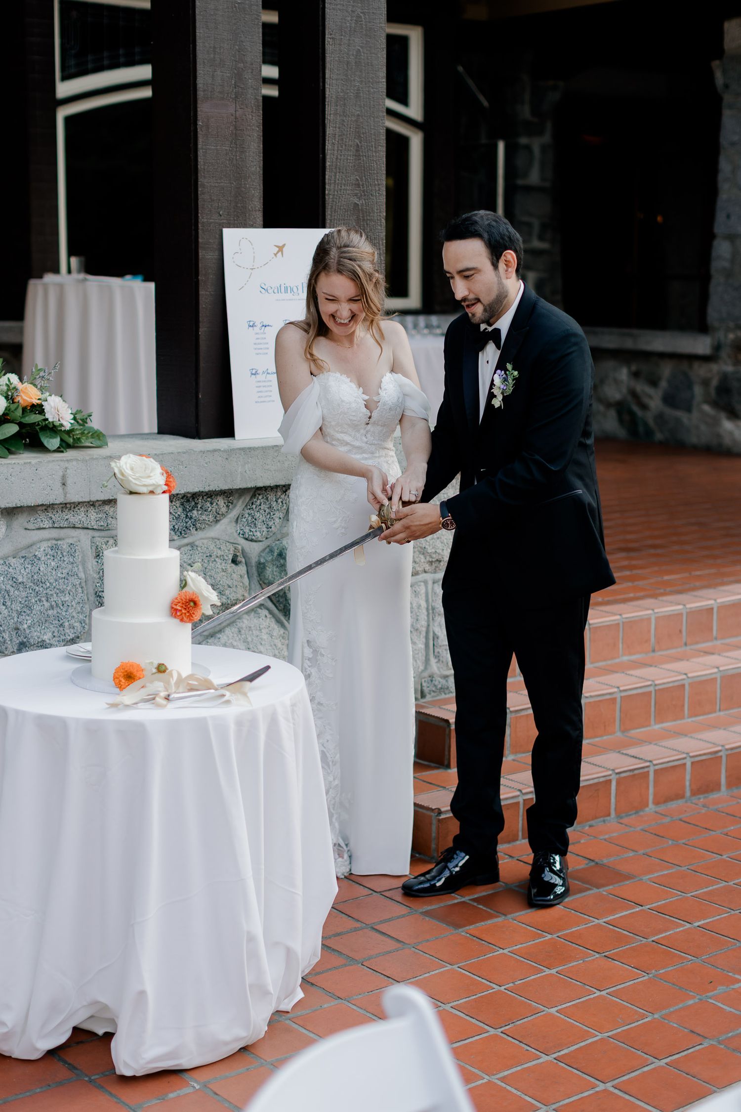 A couple cuts their elegant white wedding cake together on a terracotta tile patio during their reception celebration.