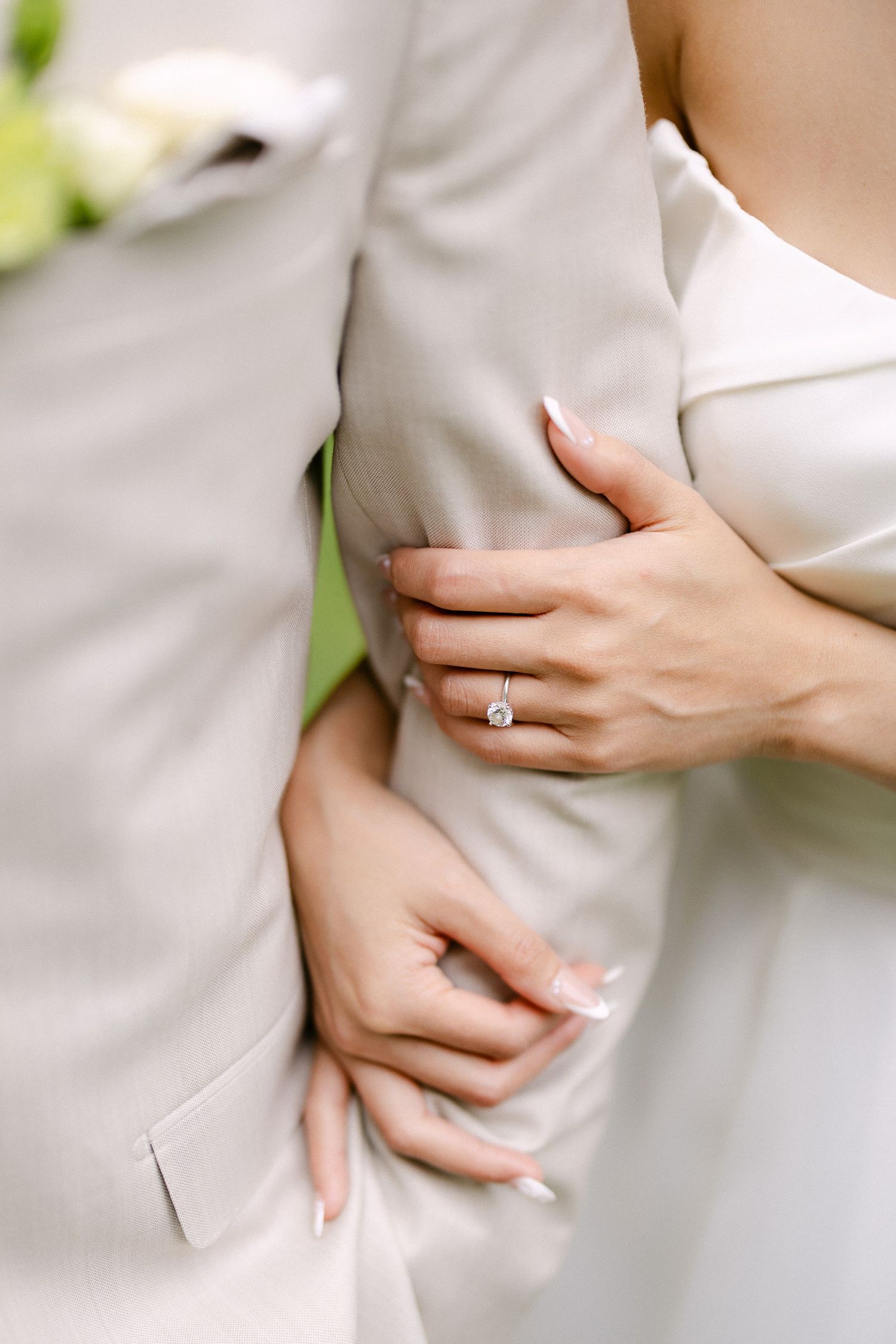 Close-up of bride and groom embracing, showcasing a stunning solitaire diamond engagement ring on the bride's hand.