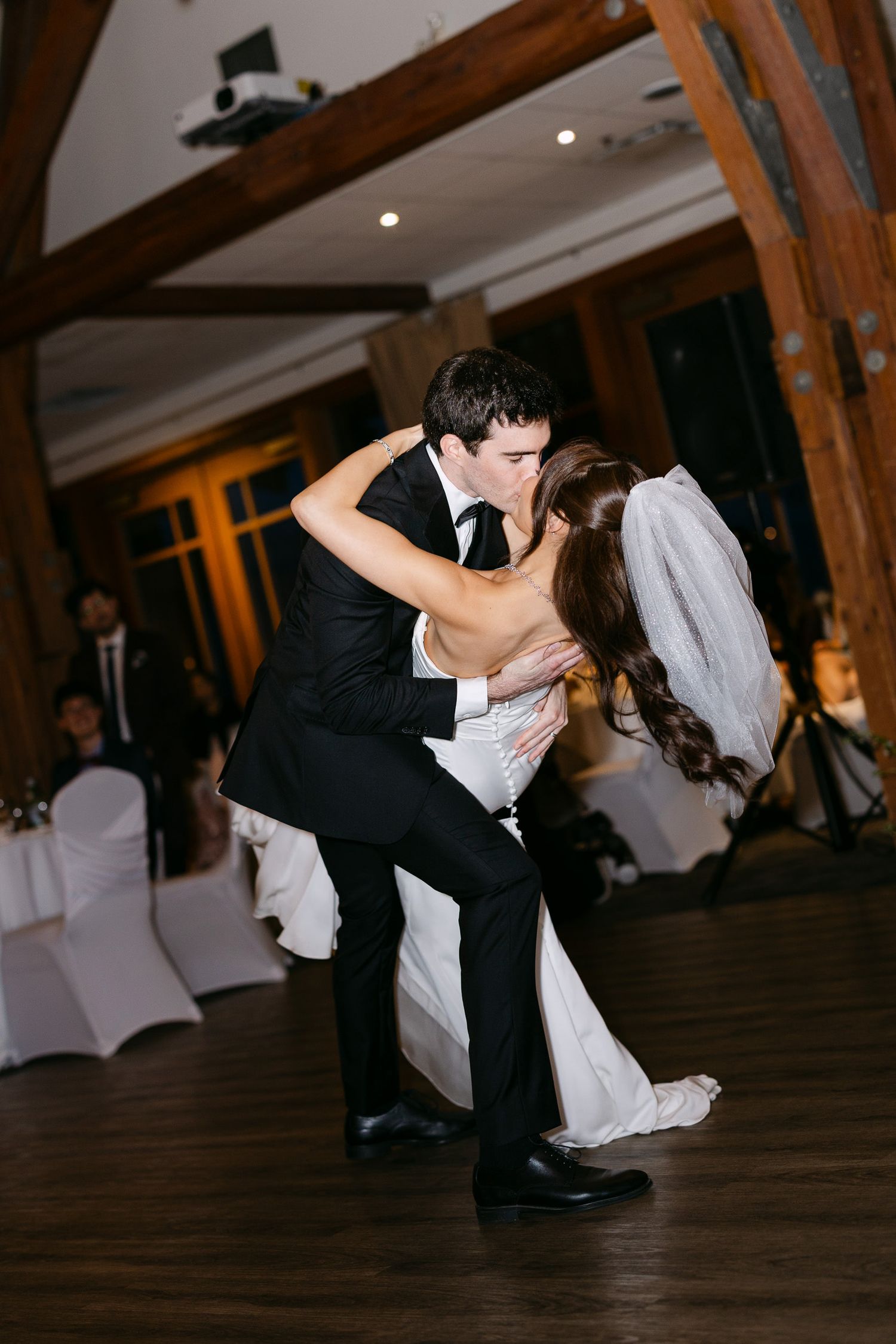 Bride and groom share a romantic dip kiss on the dance floor during their wedding reception in an elegant venue.