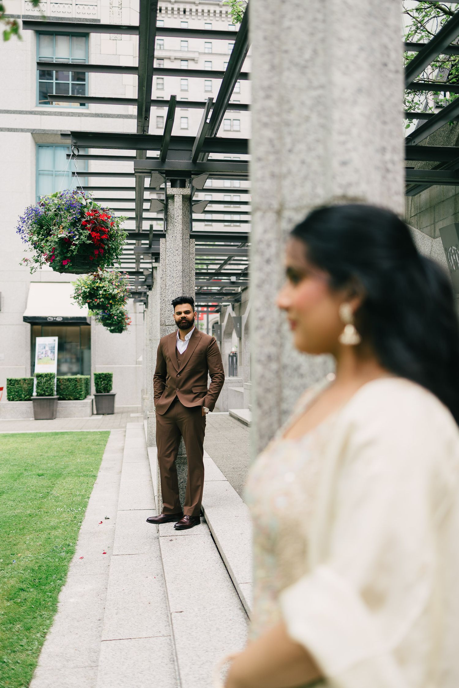 A couple poses for wedding photos in an elegant outdoor setting with white stone columns and hanging flowers.
