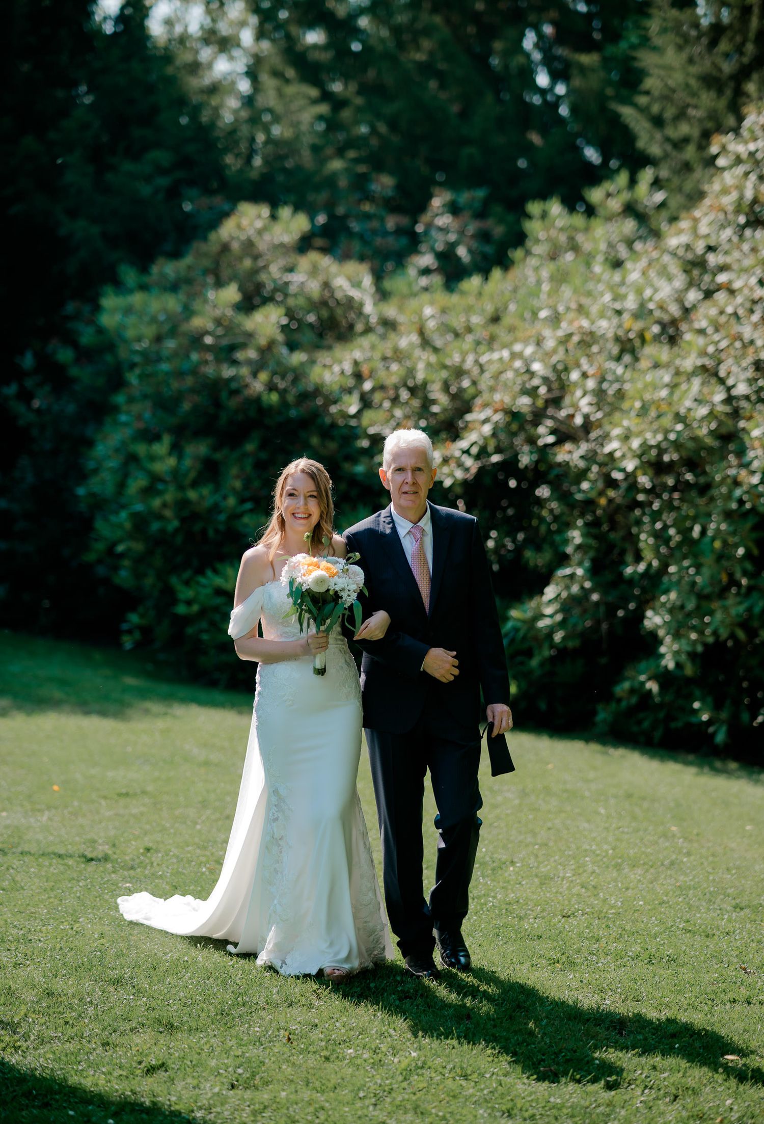 A wedding procession captured in sequence showing a bride and escort walking across a sunny green lawn with blooming trees.