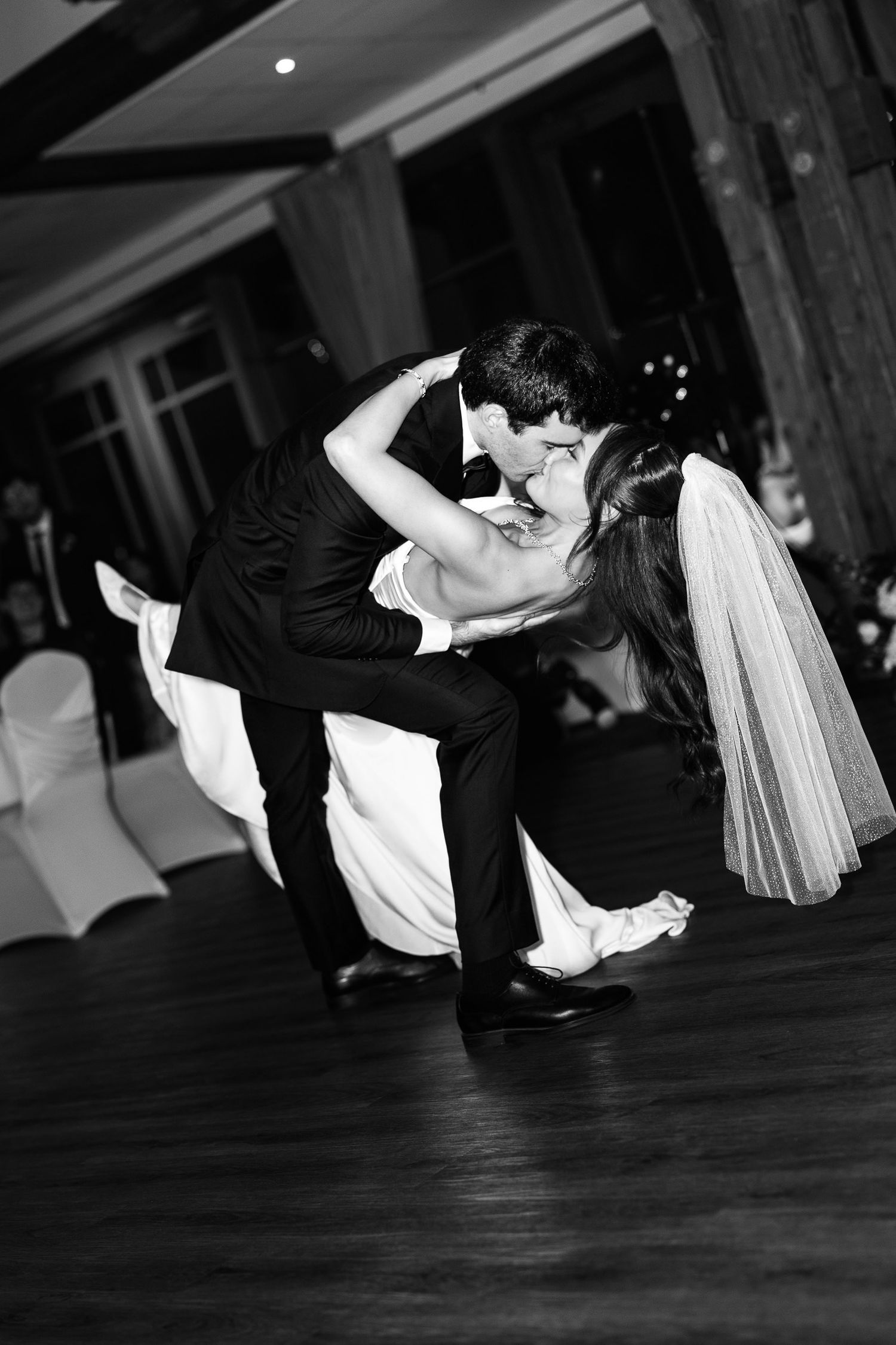 Black and white photo of a bride and groom sharing a romantic dip kiss during their first dance at a wedding reception.
