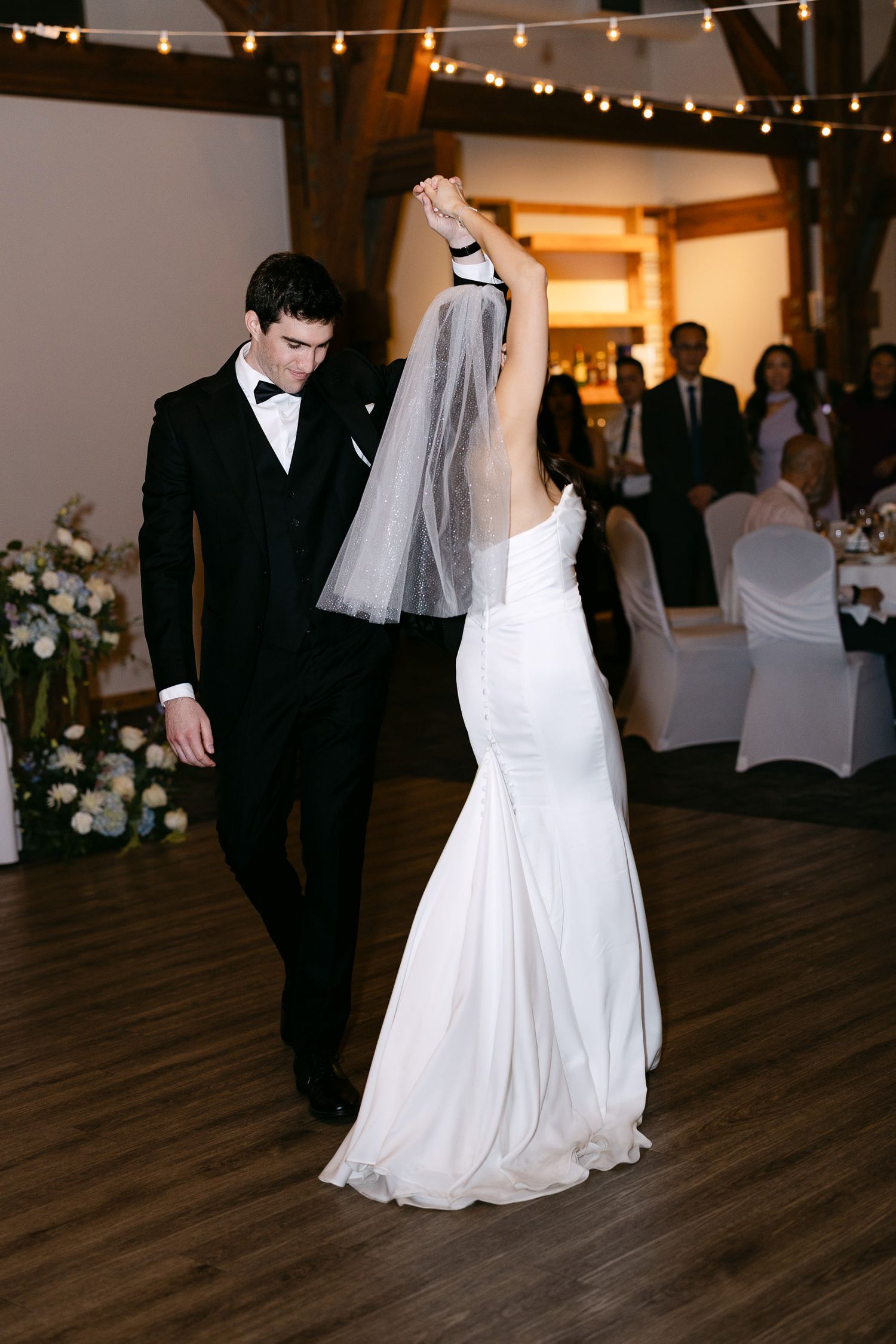 Bride and groom share their first dance, she in a white mermaid gown with veil, he in a classic black tuxedo.