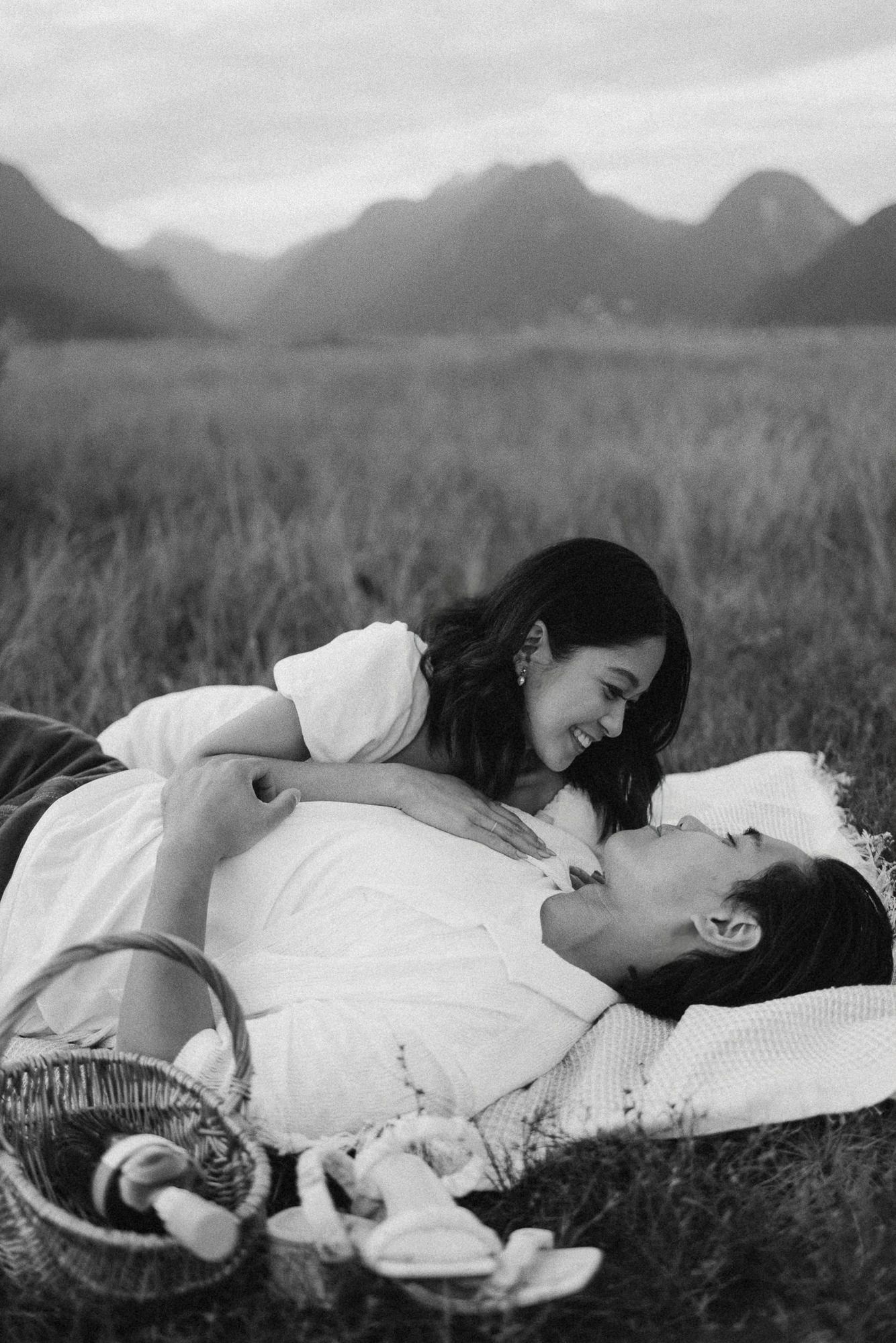 Black and white photo of a smiling woman leaning over a man on a picnic blanket with a basket nearby.