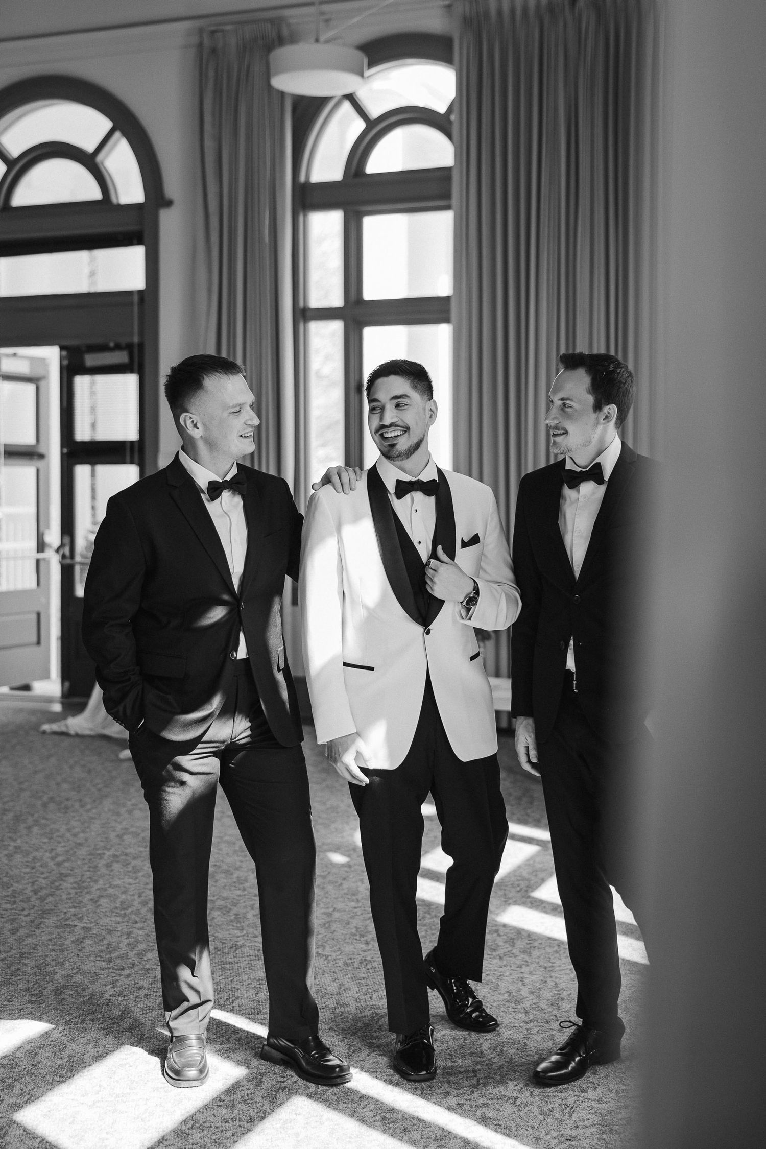 A series of black and white photos showing groomsmen in formal tuxedos standing in an elegant room with arched windows.