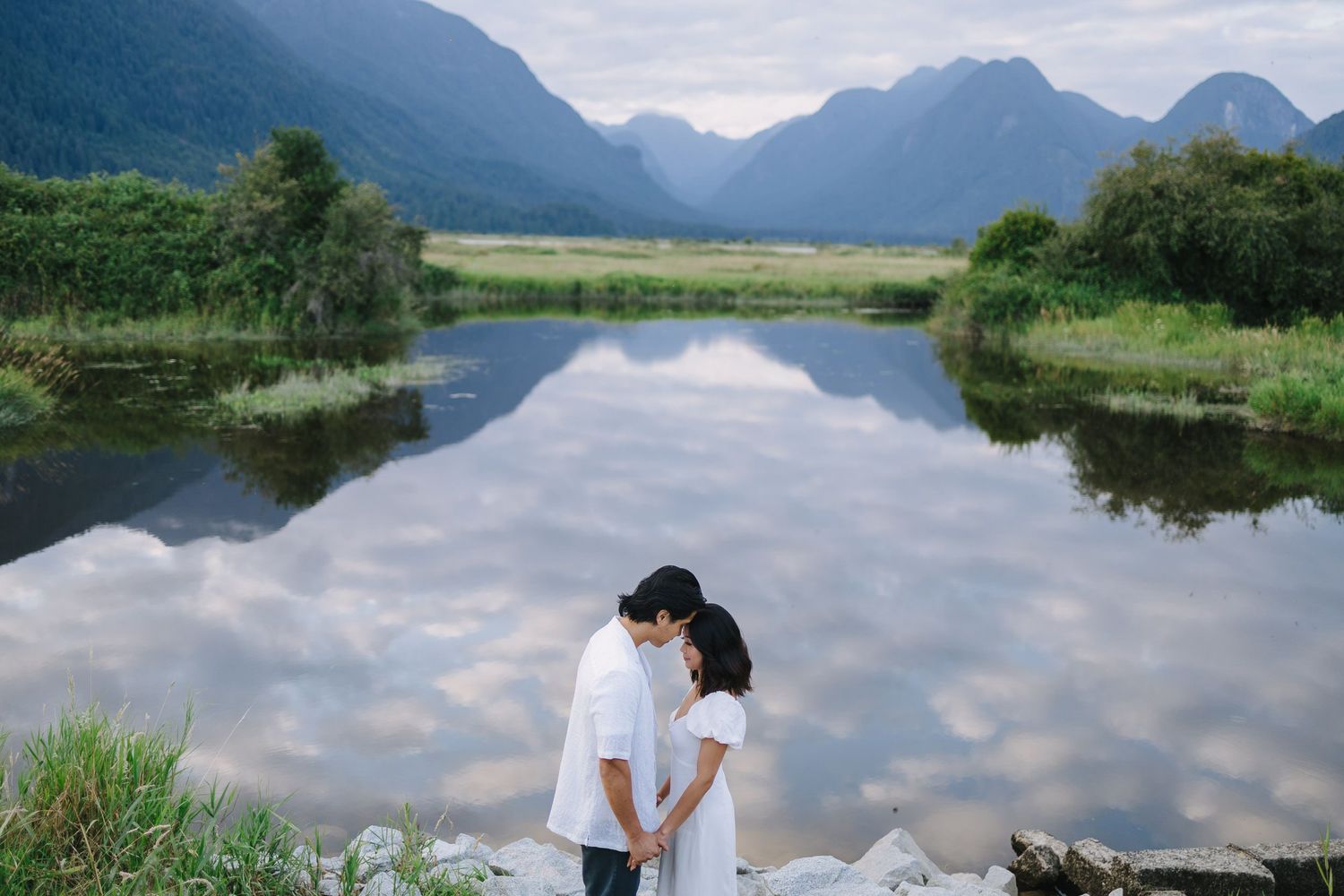 A scenic mountain lake reflects clouds and peaks with lush greenery along the shoreline in New Zealand.