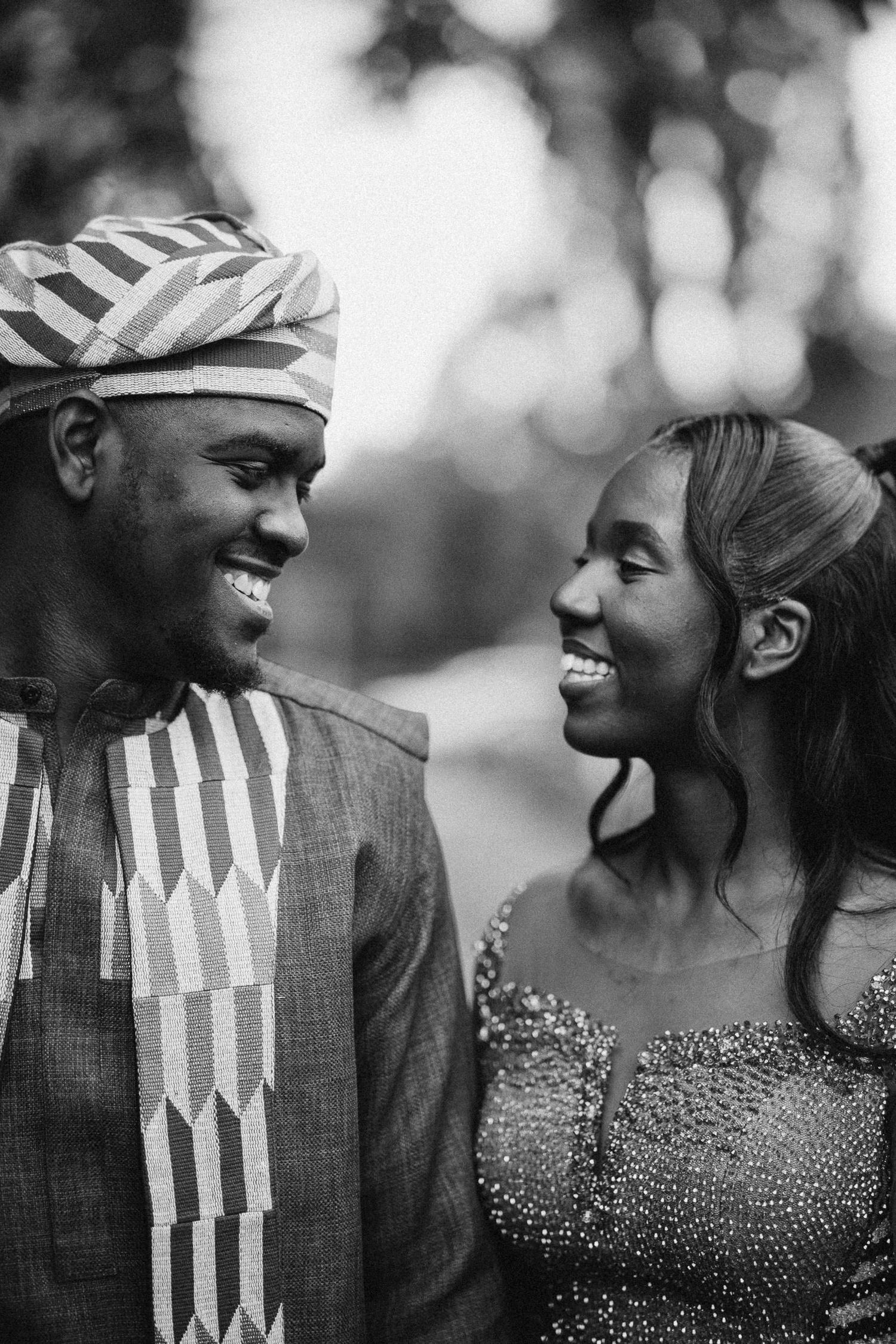 Black and white portrait of a couple in traditional African attire sharing a joyful moment together.